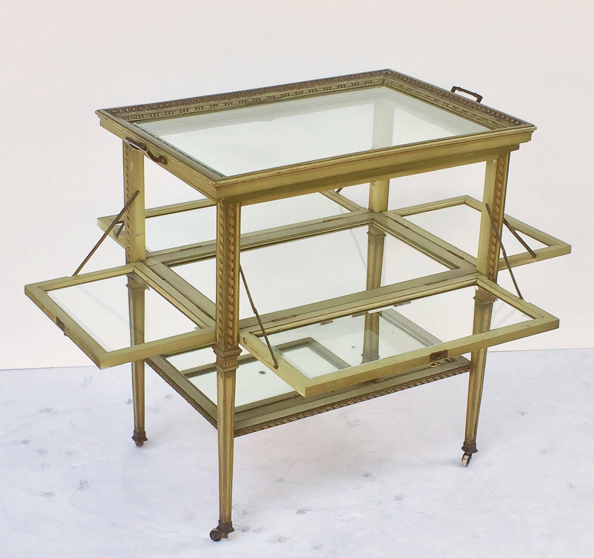 A fine Italian drinks cart or tea and coffee serving table of painted wood, featuring a large removable rectangular tray top with a moulded edge surrounding beveled glass, set upon a table base with a fitted glass top and bottom, with decorative