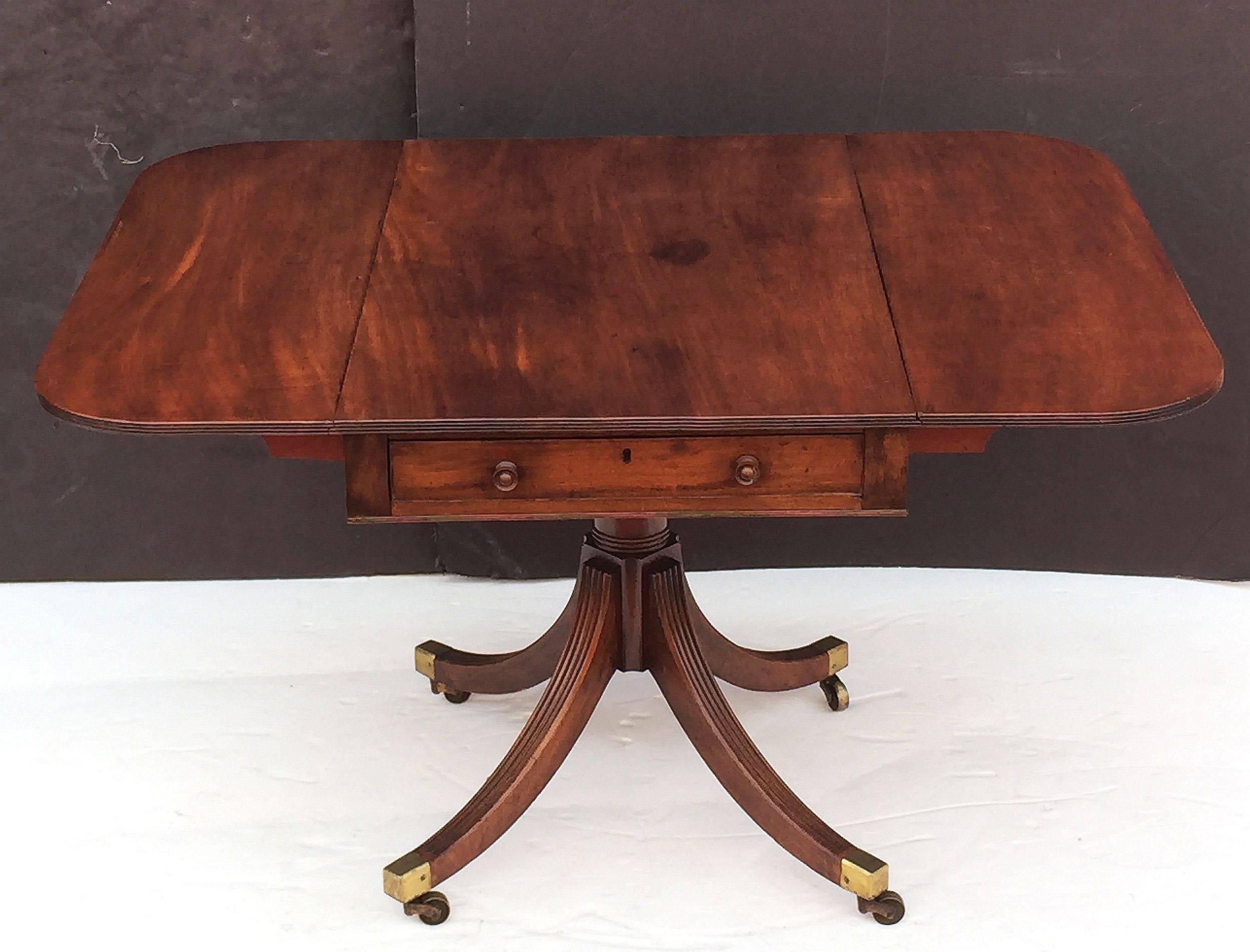 A fine English drop-leaf Pembroke table of Cuban mahogany, featuring a handsome rectangular top with fold-down sides, over a frieze with drawer and opposing faux drawer, set upon a baluster stem and four splay legs (on brass casters) - a