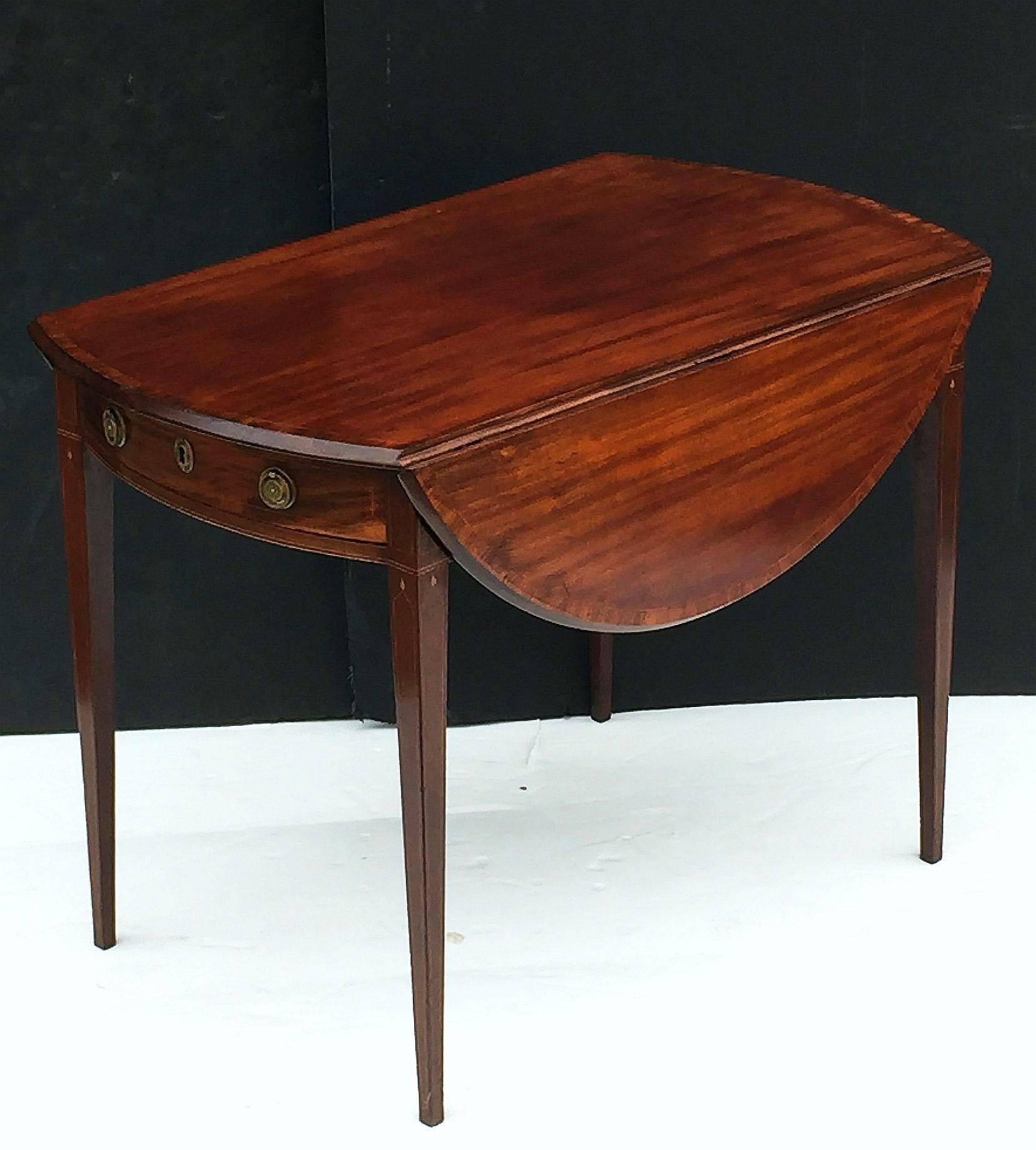 A fine English drop-leaf Pembroke table of mahogany in the manner of Sheraton, featuring a handsome oval top with crossbanding and fold-down sides, over a frieze with strung inlay, bowed drawer, and brass hardware, set upon four tapering legs with