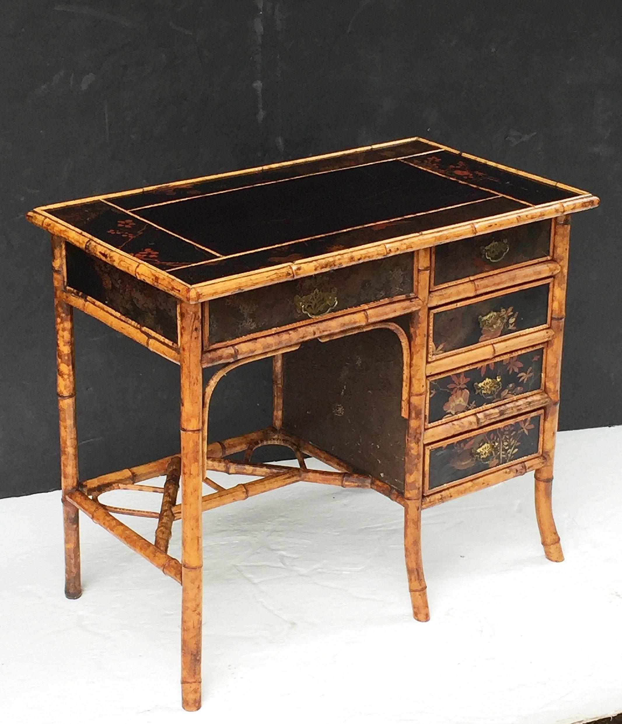 A fine English bamboo writing desk or table from the Aesthetic Movement era, circa 1870-1910, featuring a rectangular top of lacquered panels and bamboo accents surrounding a leather writing surface.
Over a frieze of five drawers and a knee-hole