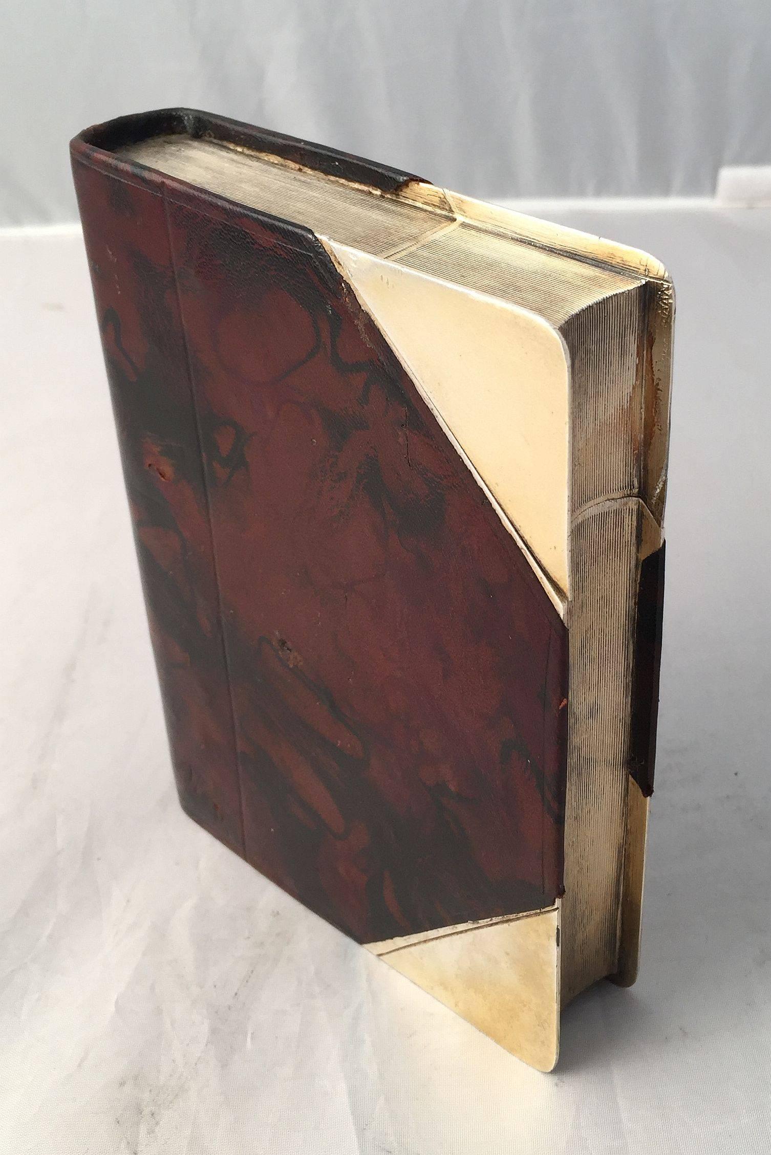 A rare English drinks or liquor flask, by James Dixon and Sons, Ltd. of Sheffield, featuring a book-shaped body of leather over gilt metal, holding eight ounces, with a removable twist-off corner that functions as the flask cap. 
The binding in