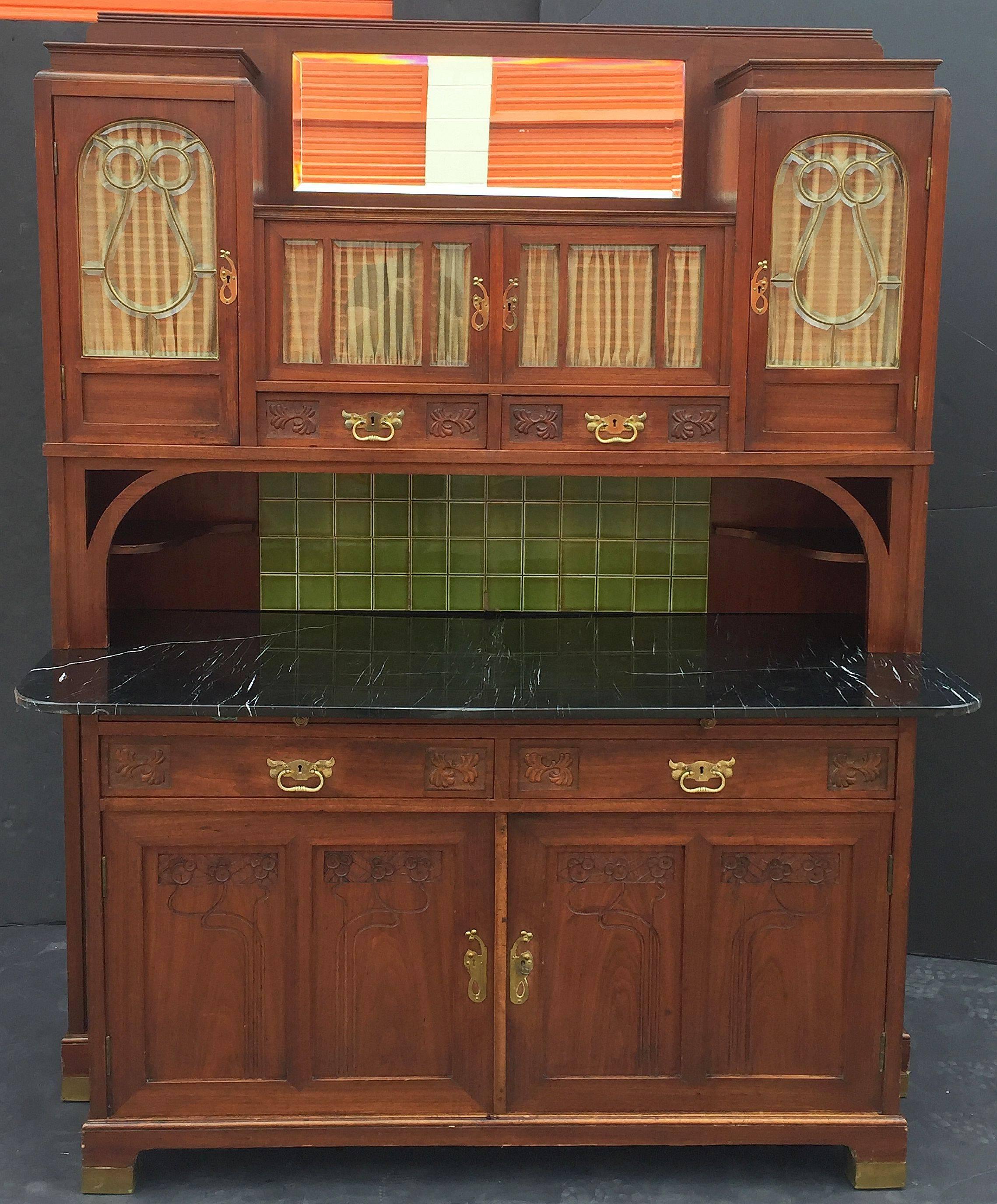 A handsome French Art Nouveau buffet cupboard or bar cabinet featuring an upper tier with a bevelled mirror and four glazed cupboards over two drawers, and green-glazed tiles backsplash with two opposing corner shelves. 

The bottom tier cabinet