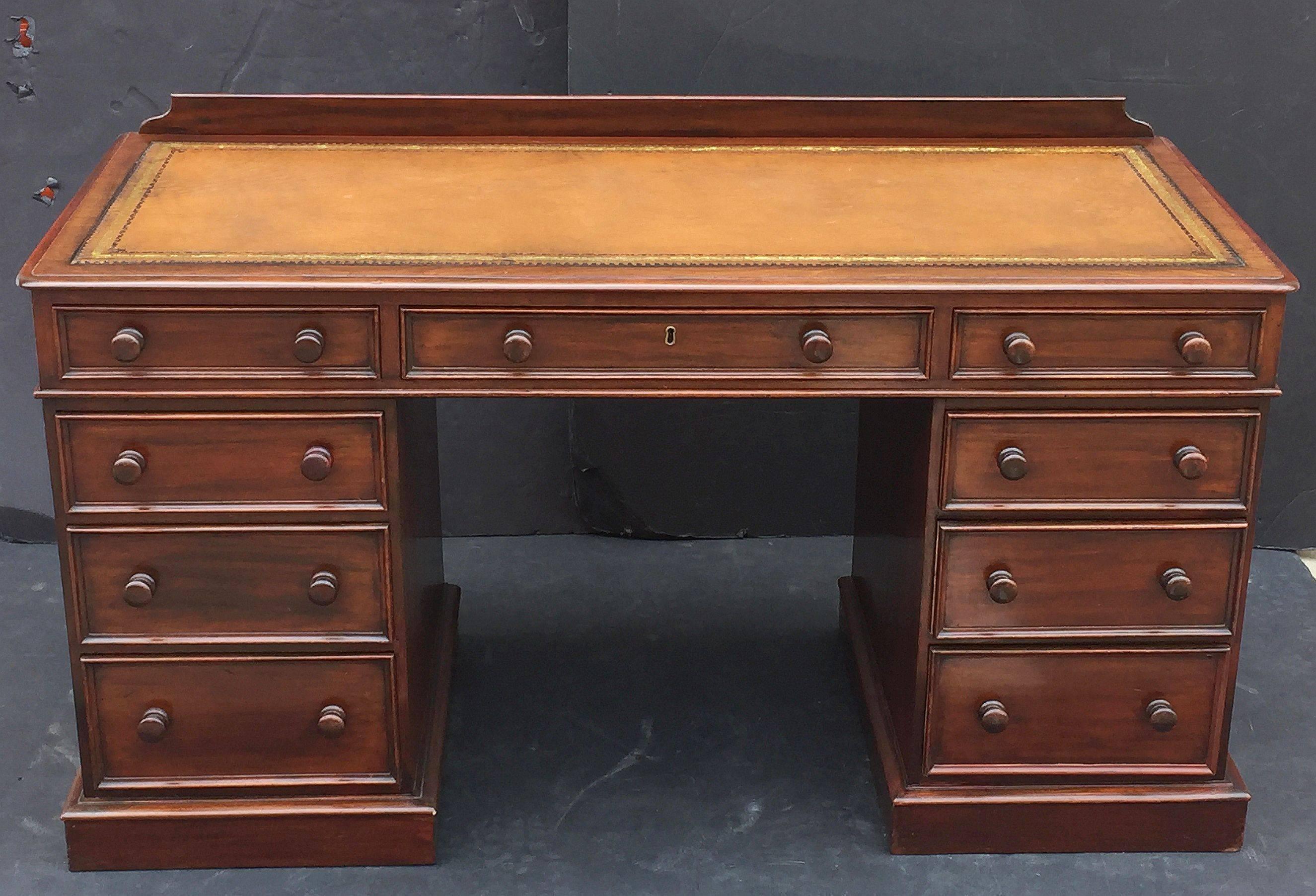 A fine English pedestal desk or writing table of mahogany, featuring an embossed leather top with backsplash gallery, with a frieze of two opposing beaded small drawers surrounding a beaded center long drawer with brass escutcheon and key. Set upon