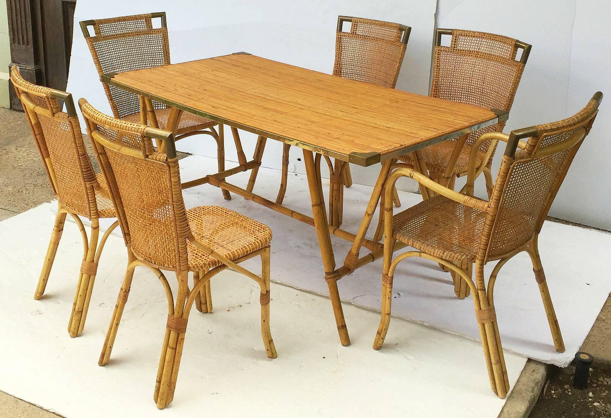 A fine French rattan and bamboo table and rattan chairs set from the mid-20th century, featuring a large rectangular table with brass-bound rattan top set upon a stylish bamboo stretcher base, two armchairs with brass-bound corners on the backs and