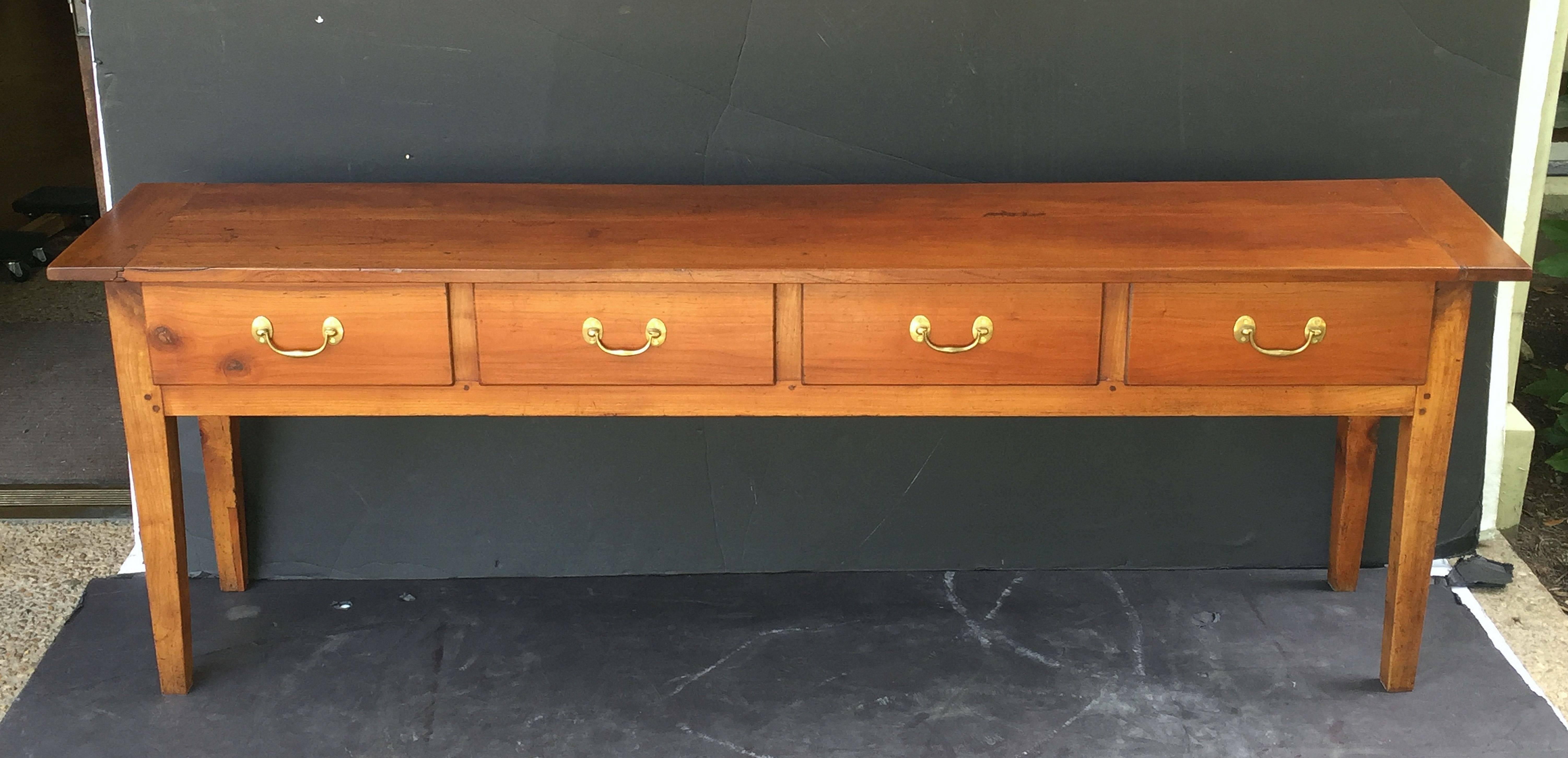 A handsome French console sideboard (or serving table) of cherry wood featuring a rectangular plank top over a large frieze with four drawers, each with brass hardware pulls, paneled back and sides, and resting on tapering square legs.