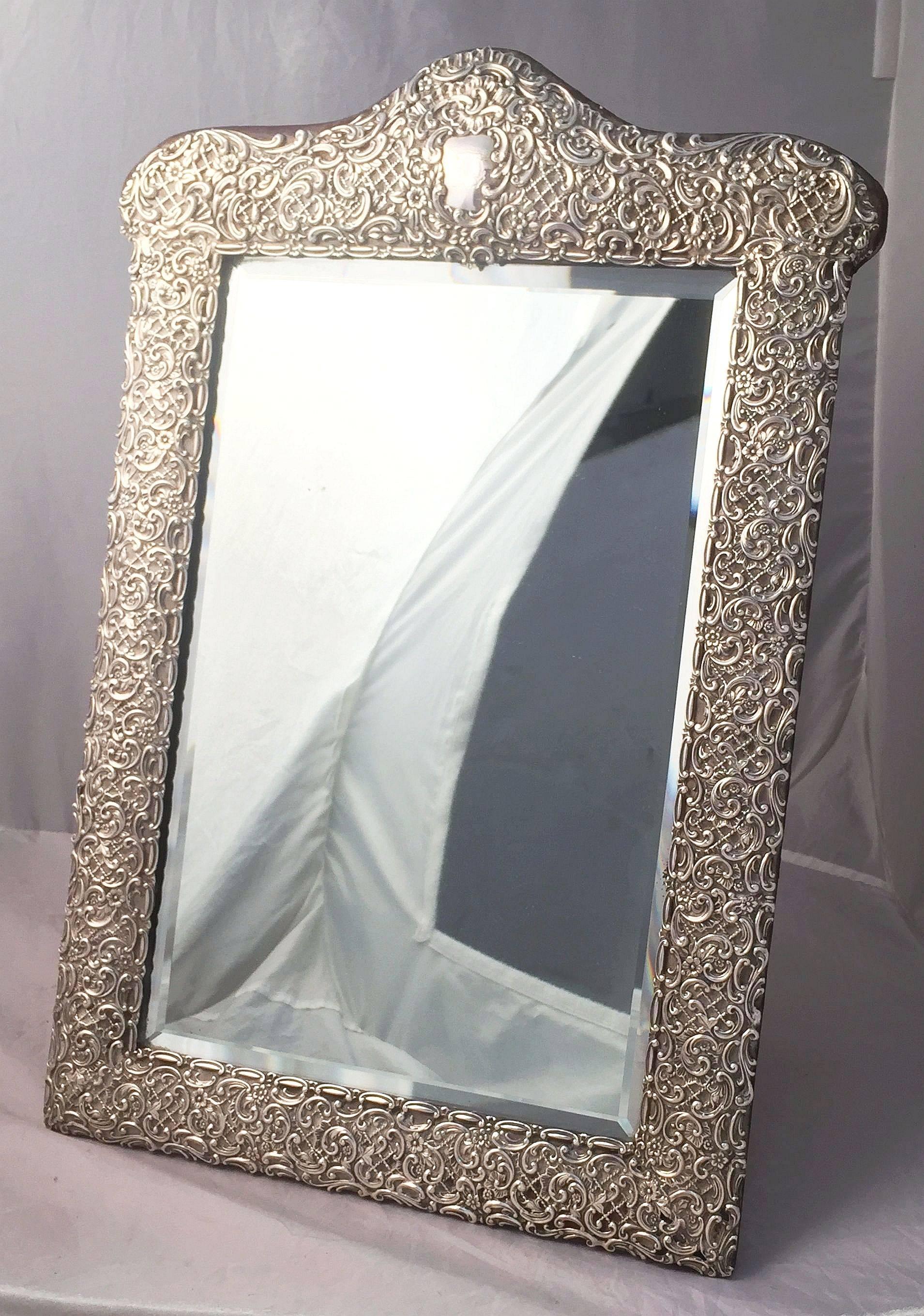 A fine English vanity or tabletop mirror of Sterling silver, featuring a chased Rococo scroll relief design to the frame, enclosing a rectangular beveled mirror, back of felt covered wood with folding Stand.

Hallmarks for Birmingham, circa