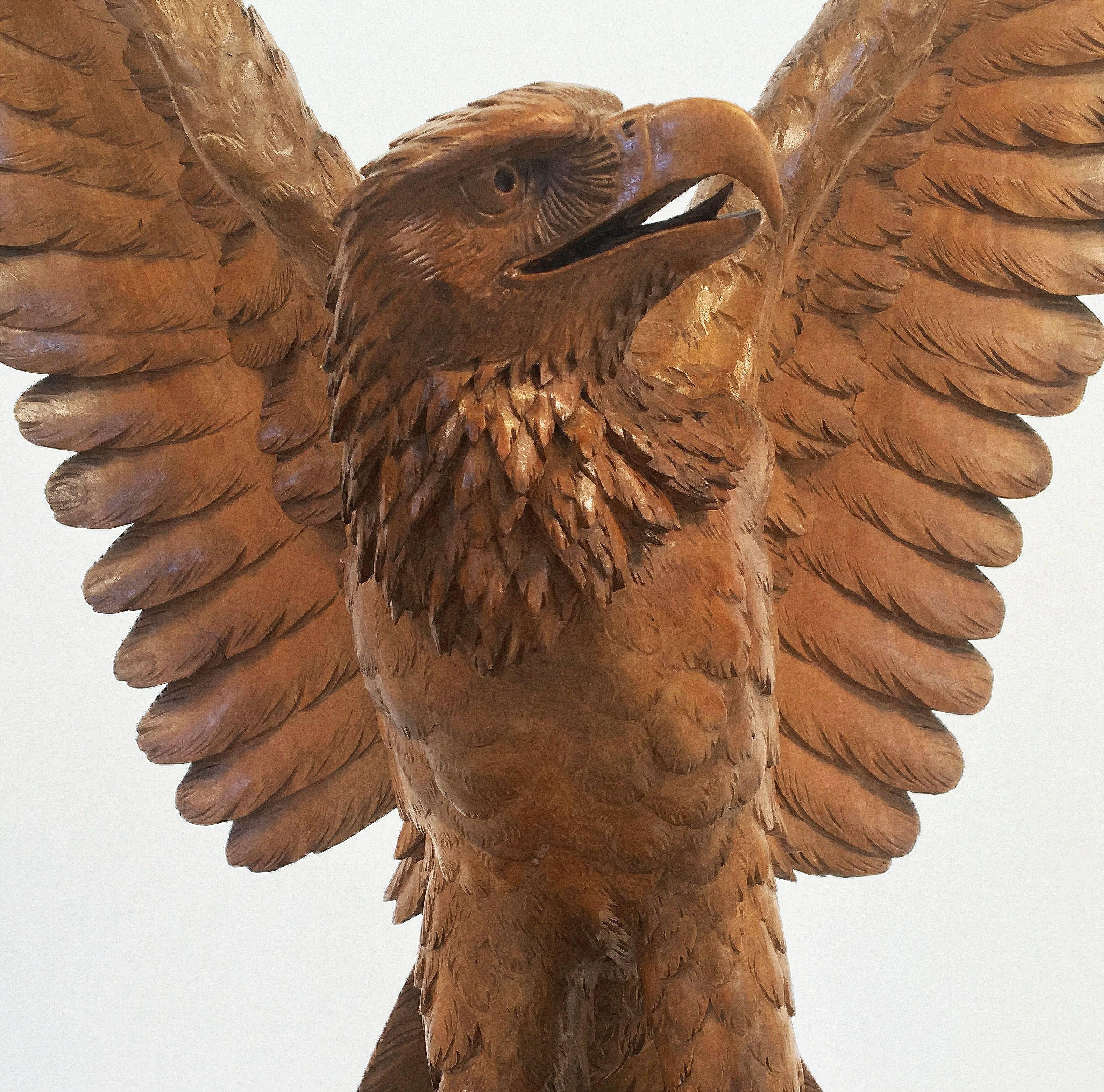 A large Black Forest Eagle sculpture of carved wood, in a standing pose with outspread wings, on platform base styled as a boulder. 
Featuring fine detail to the head, body, wings, and base. 

Bearing label 