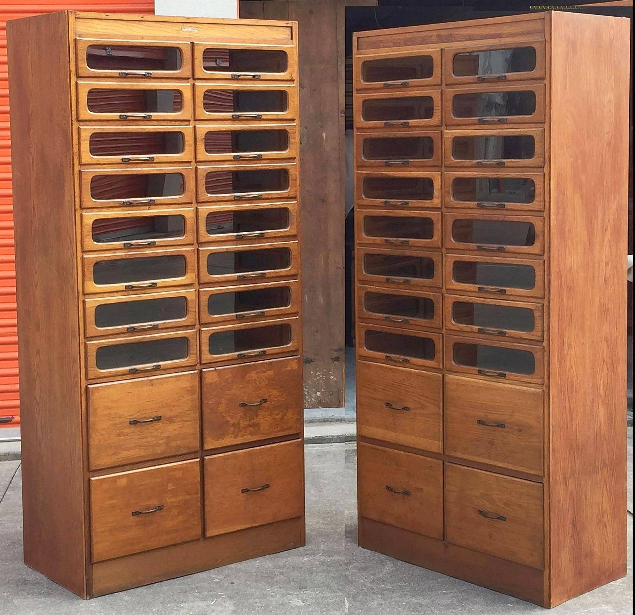 An exceptional pair of large haberdashery or haberdasher's cabinets from England featuring:

16 glass fronted drawers over four blind cupboard drawers .20 drawers total on each cabinet.

The fitted drawers with steel hardware.

Label at top
