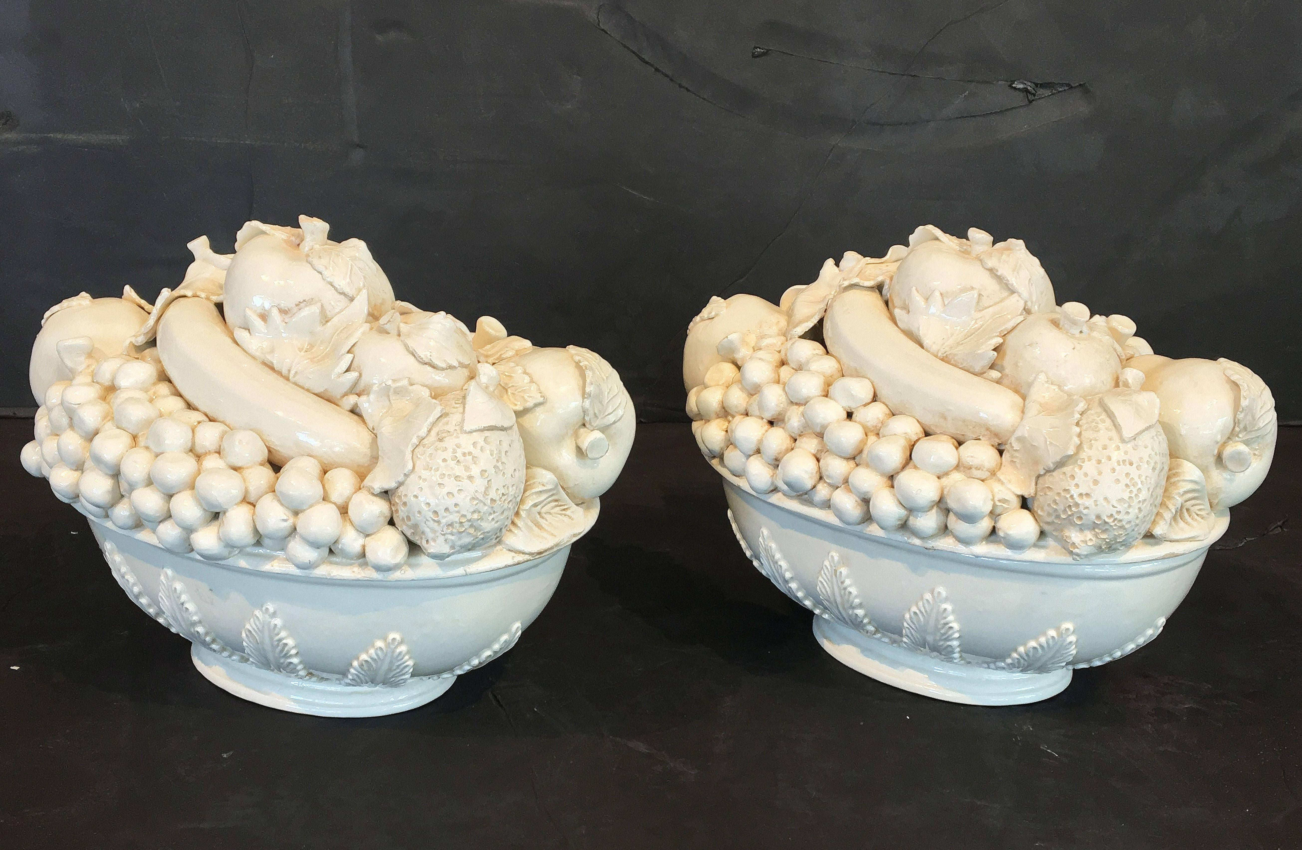 A fine pair of Italian creamware or white glazed oval ceramic bowls of fruit, each featuring a fitted lid with a relief of fruit including apples, grapes, and pomegranates over an oval raised pedestal bowl base. 

Great for serving or for use as a