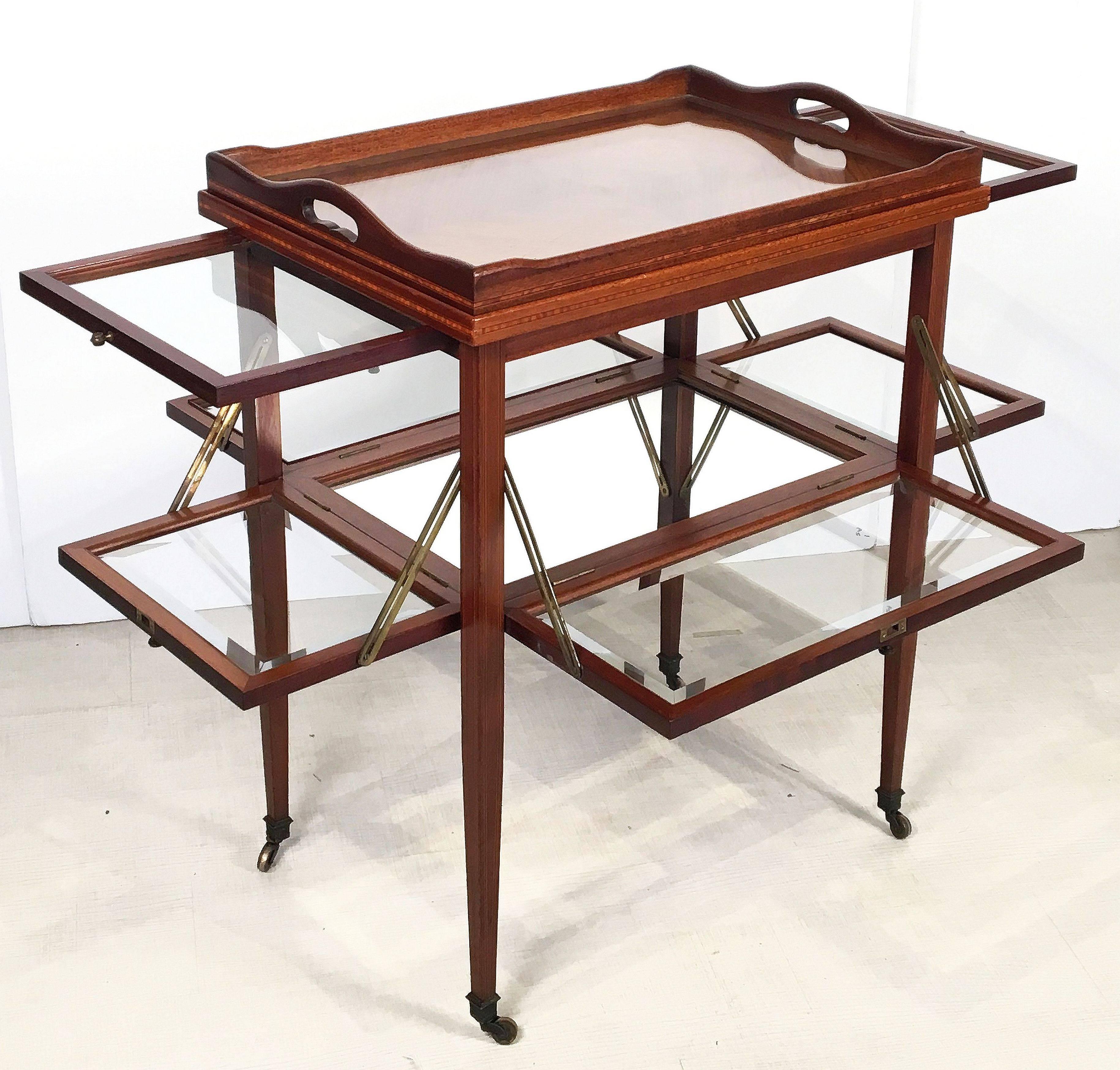 A fine English drinks cart or tea and coffee serving table of inlaid mahogany from the Edwardian era, featuring a large removable rectangular tray top with a moulded edge surrounding beveled glass, set upon a table base with a fitted parquetry top