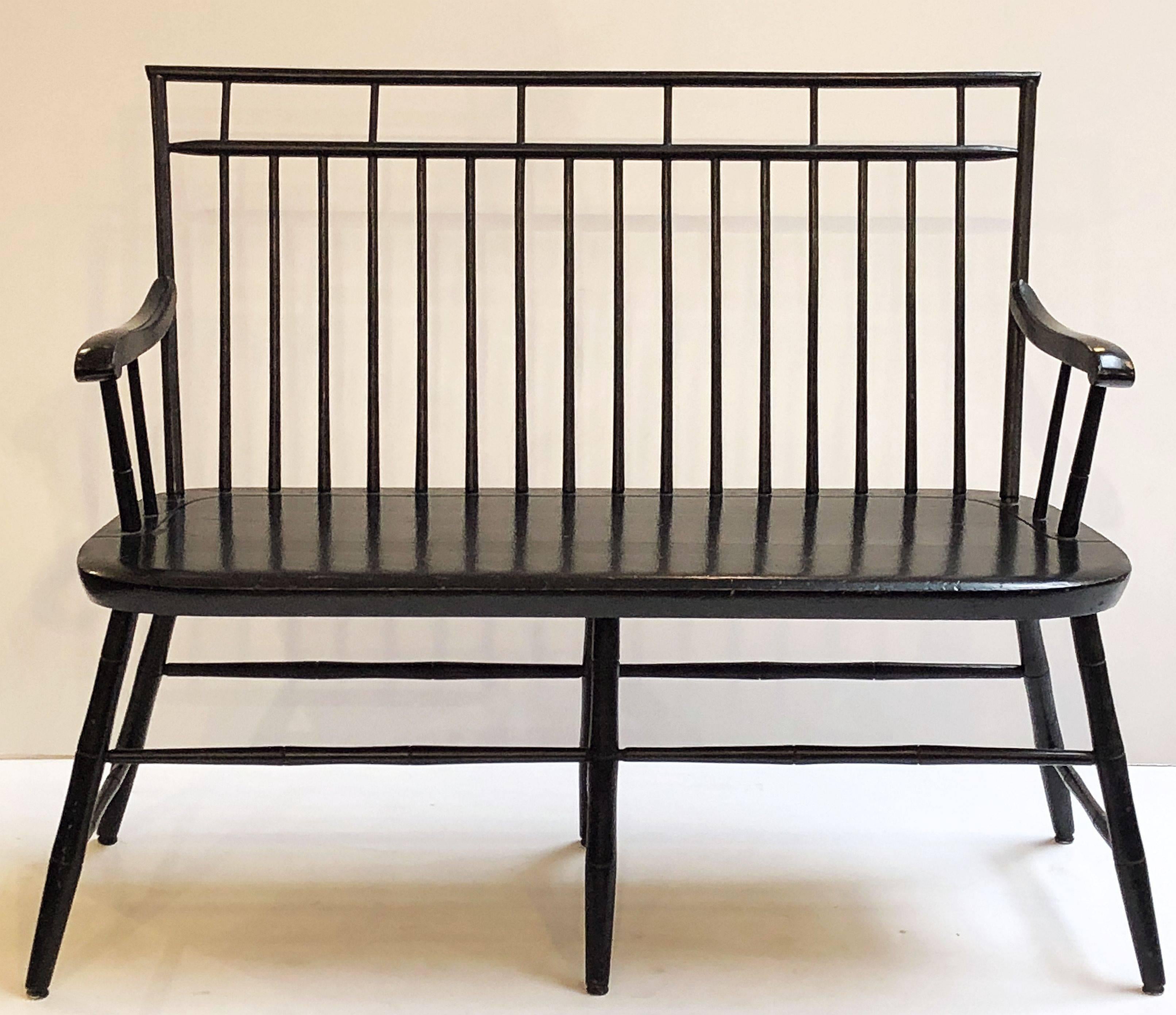 A fine American settee or seating bench of black-painted wood, featuring a spindle back, serpentine arms, mounted to a comfortable seat with turned leg supports.