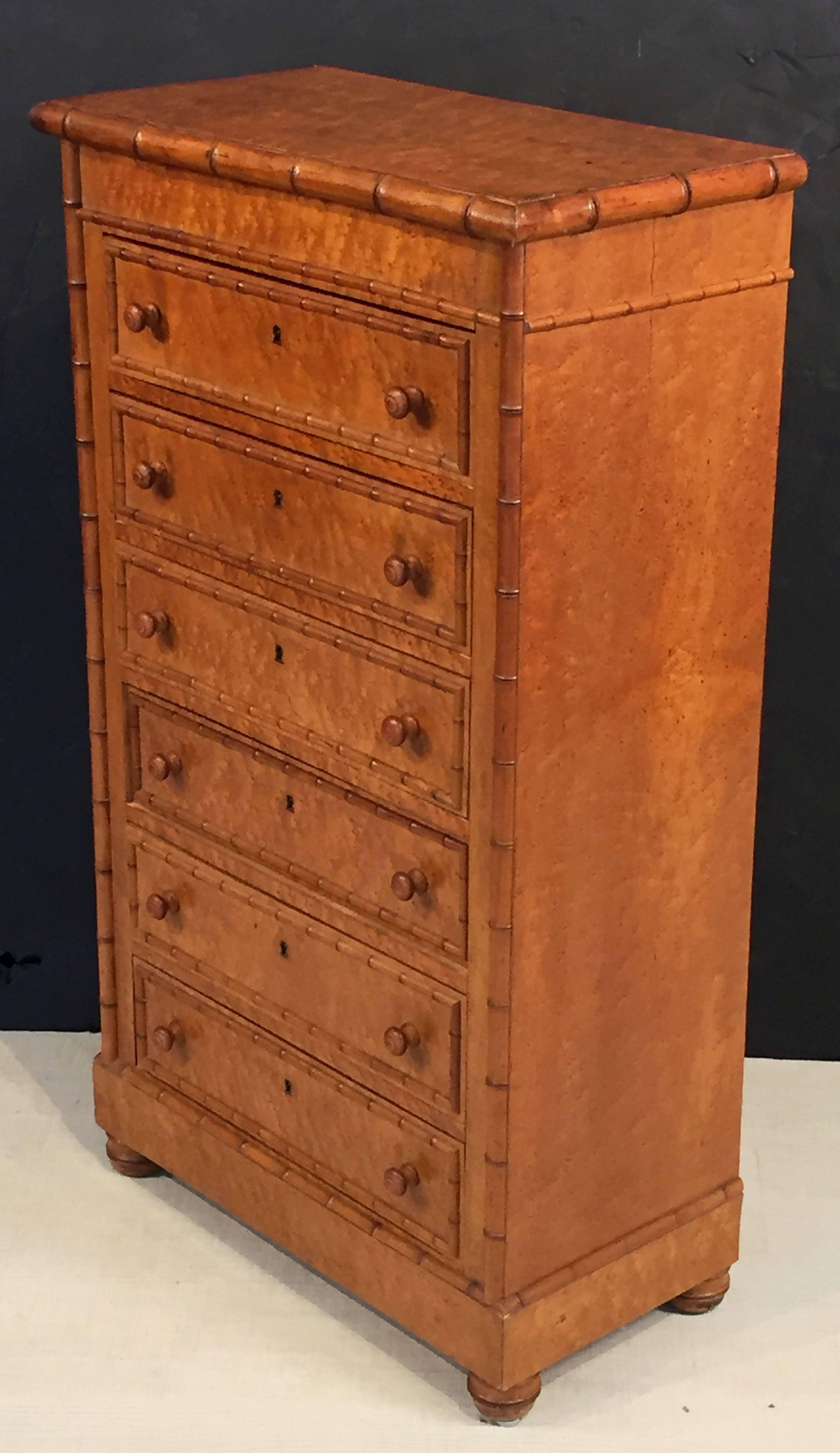 A fine English collector's cabinet or chest of faux bamboo and figured curly or bird's-eye maple, fondly known as a Wellington, featuring a moulded top over six drawers, with decorative faux bamboo accents, turned knobs, and escutcheons, on four