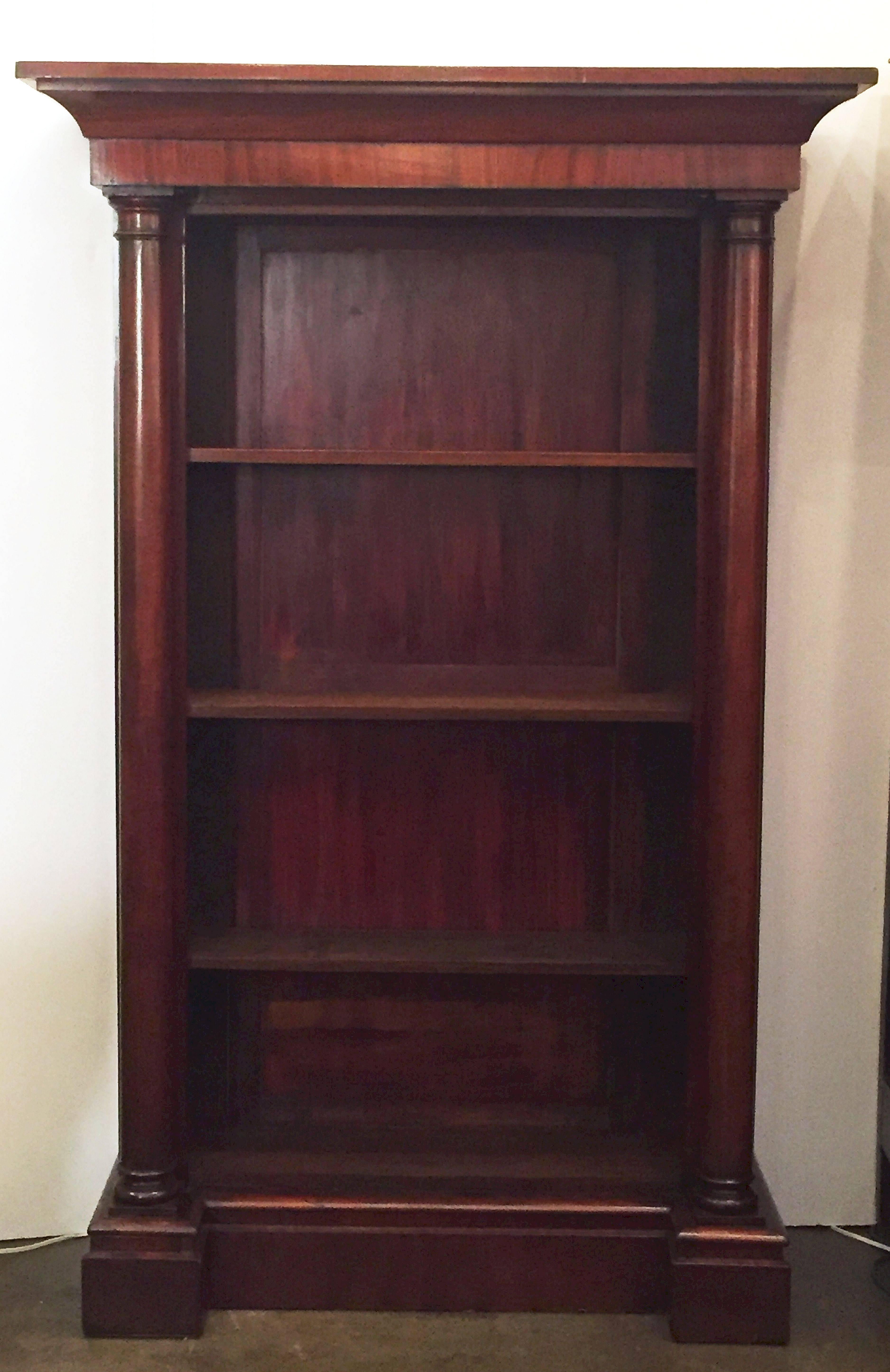 A handsome large English open bookcase of mahogany, featuring a crown moulding top frieze over three adjustable shelves, flanked by two tuned column supports, and resting on a raised plinth.