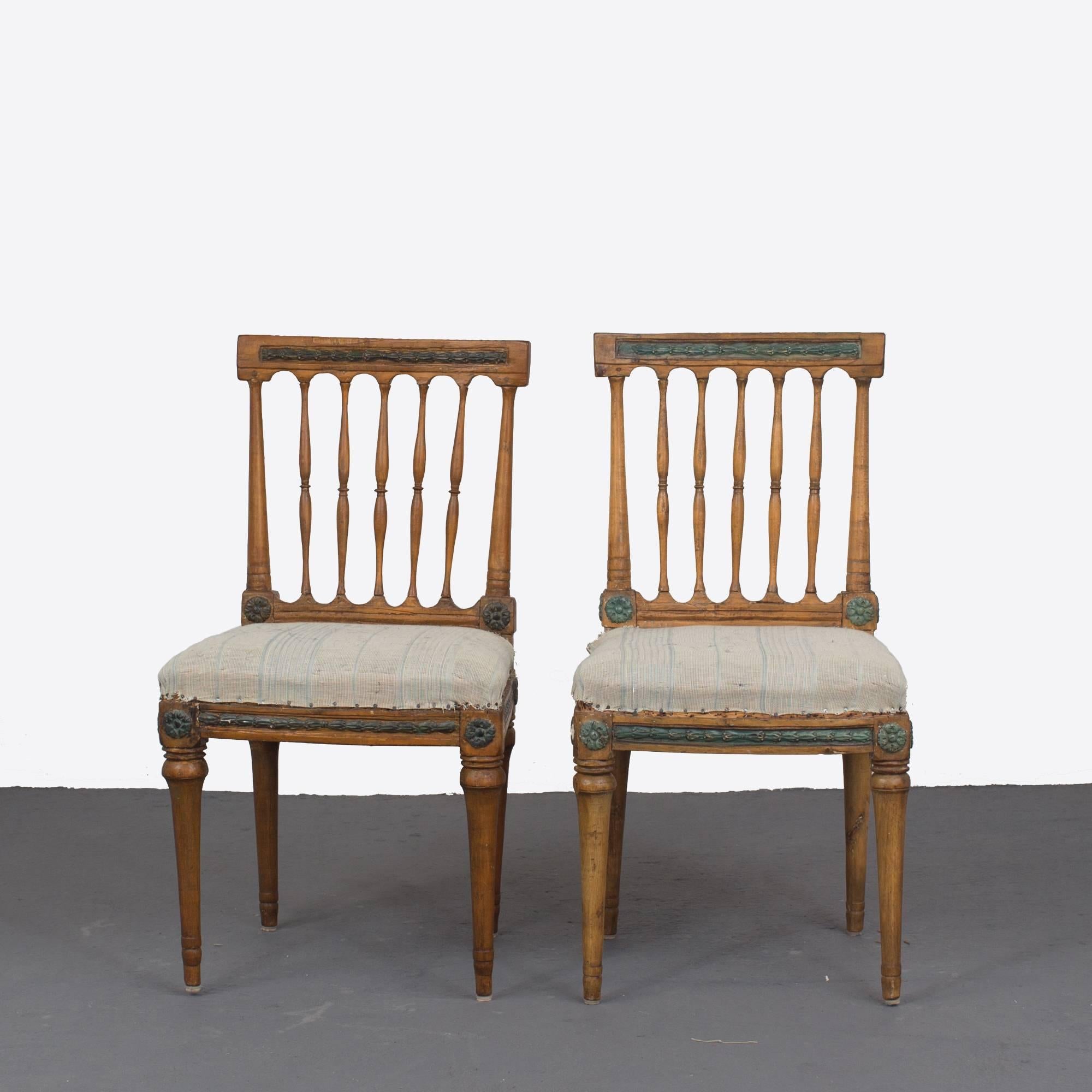 A pair of side chairs made during the Gustavian period 1790-1810. Frame made in stained wood with dark green details. Open back with five spindles and a loose cushion seat. Frieze with carved details resting on rounded channeled legs.