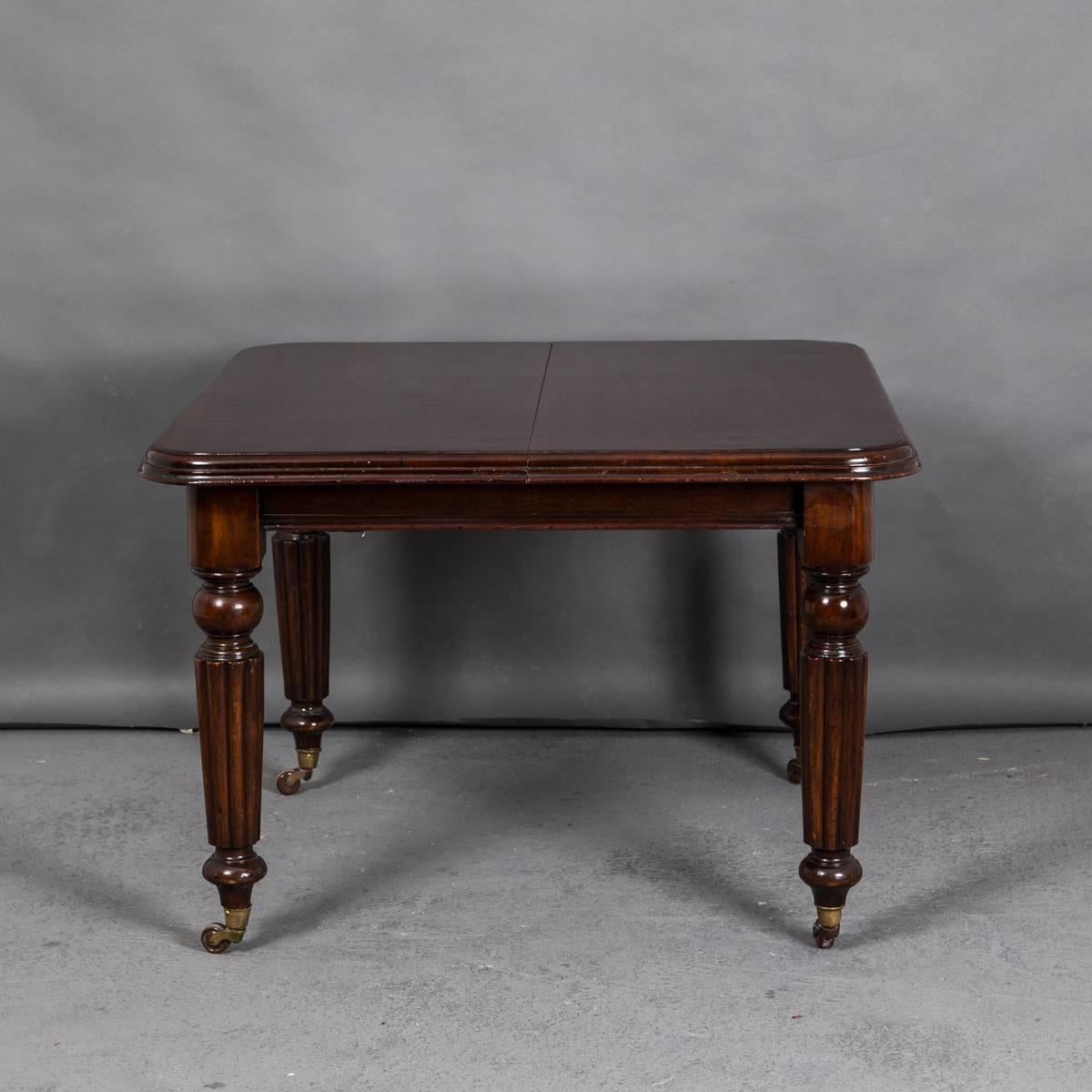 An elegant dining table made in England from polished dark brown mahogany. Extendable with one leaf (as in picture) of 18.2 in. Rounded and channeled legs ending with brass casters. Reeded edge of top. 