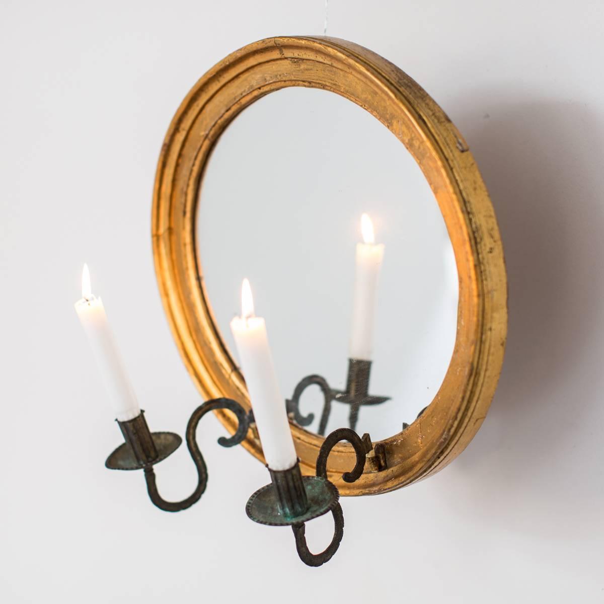 Wall sconce mirror oval giltwood French, 19th century, France. An oval mirrored wall sconce in giltwood made in France during the early 19th century. Two candleholders in oxidized copper. Original gilding and mirror glass.