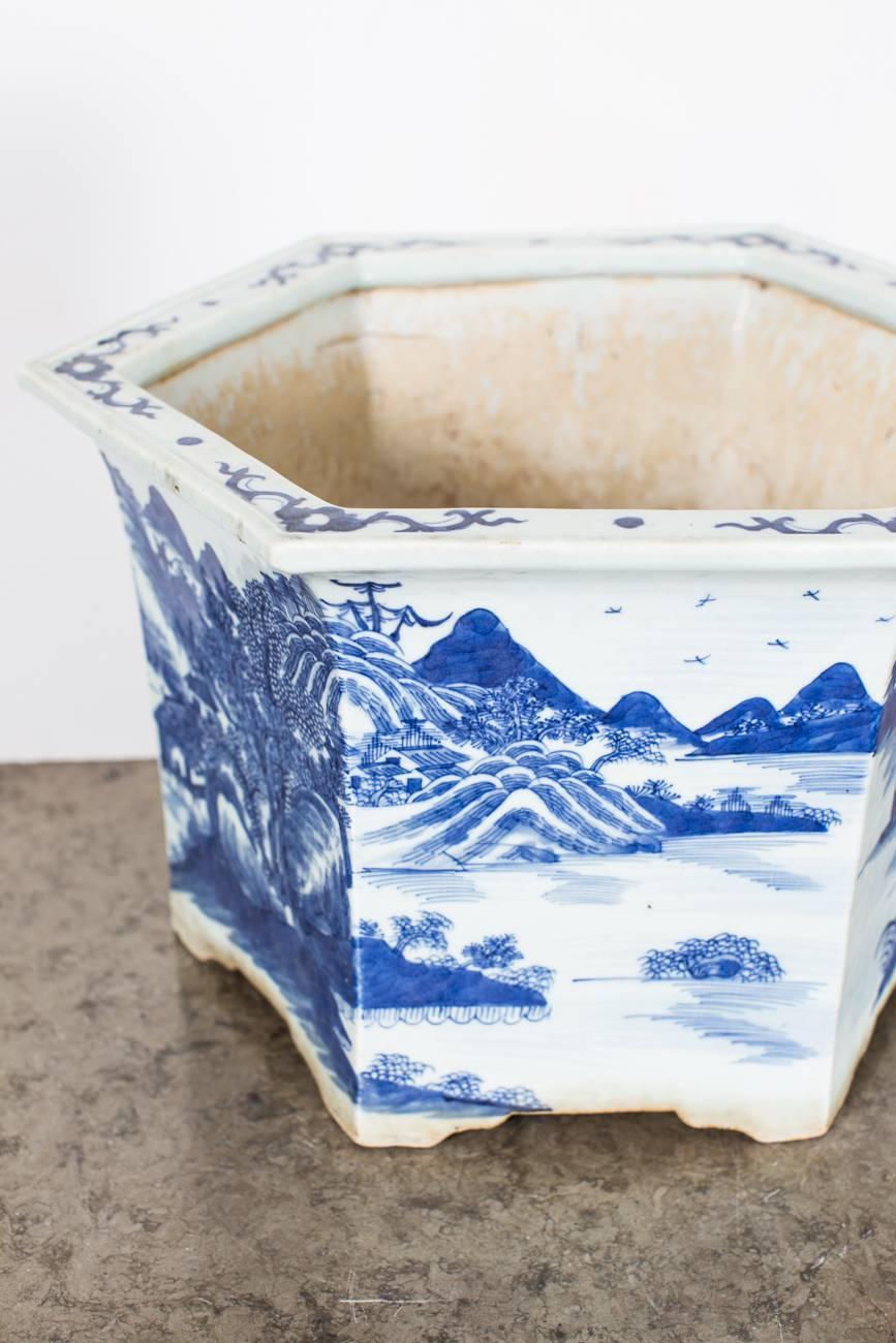A jardiniere made during the 19th century in China in a hexagonal shape. Blue and white porcelain with idyllic scenes of a lake side retreat with towering mountains, serene fishermen, and contemplative scholars.