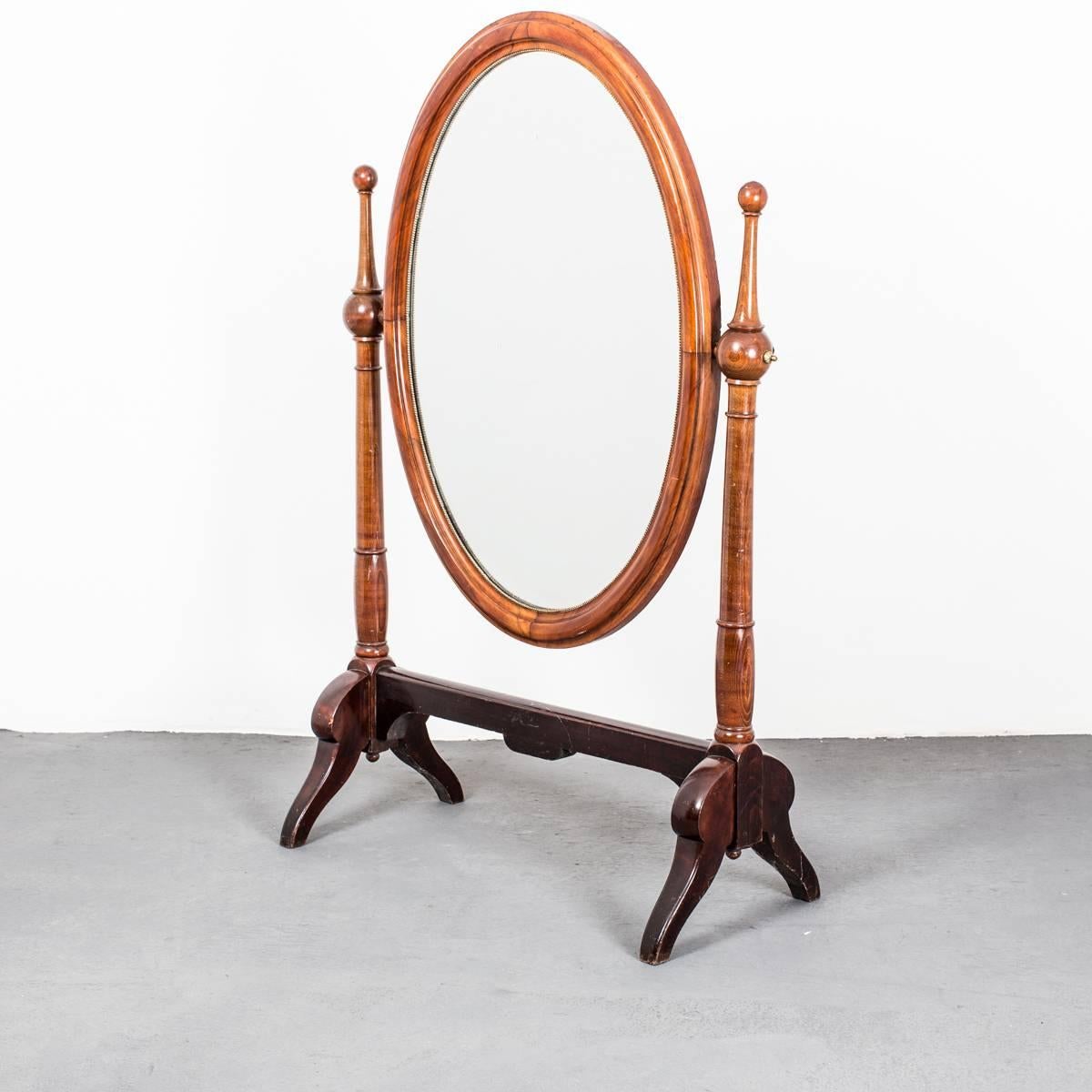 A standing mirror made during the early 19th century in mahogany. Oval shaped mirror with a pearl beaded inner edge. Details in brass.