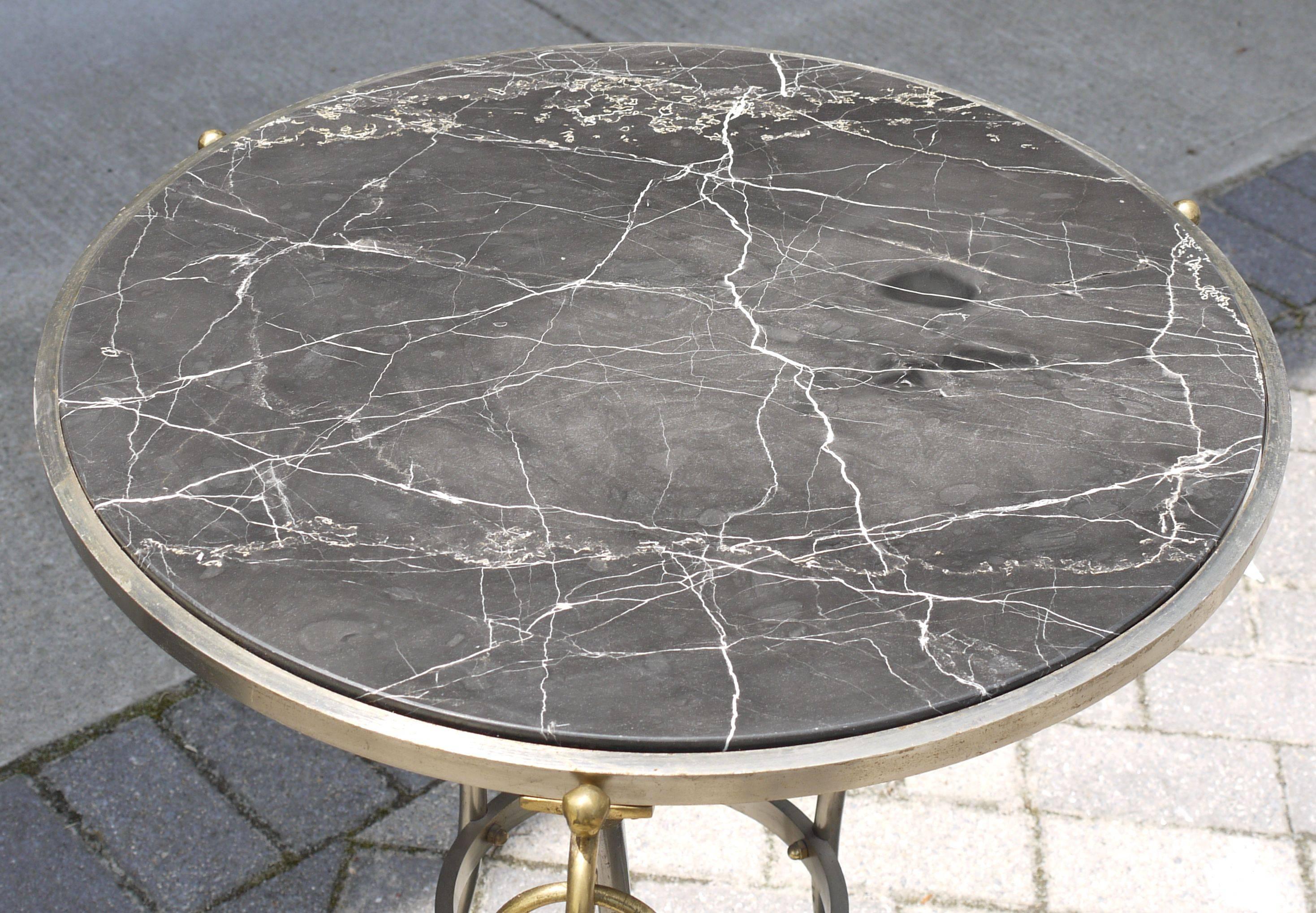 A neoclassical gueridon with nickled brushed steel finish and brass appointments topped with a black marble top that started out life as being polished but through the years has almost become a honed marble. It's the way old marble should look.