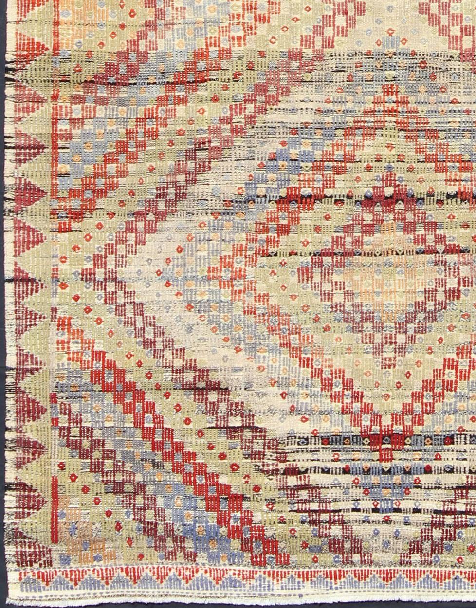 Measures: 6'9'' x 10'9''.
Featuring a large diamond pattern with a spotted and speckled assortment of geometric checkered elements, this unique vintage Kilim showcases an array of muted color tones that have been softened by age. Colors include