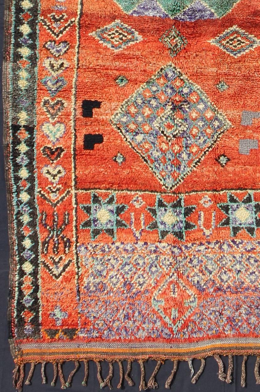 This vintage Moroccan rug is full of life and soul, featuring designs based around the lozenge and the eight-pointed star symbols. The soft orange field features tribal motifs with hints of purple, mint green, gray, charcoal and butter gold accents.
