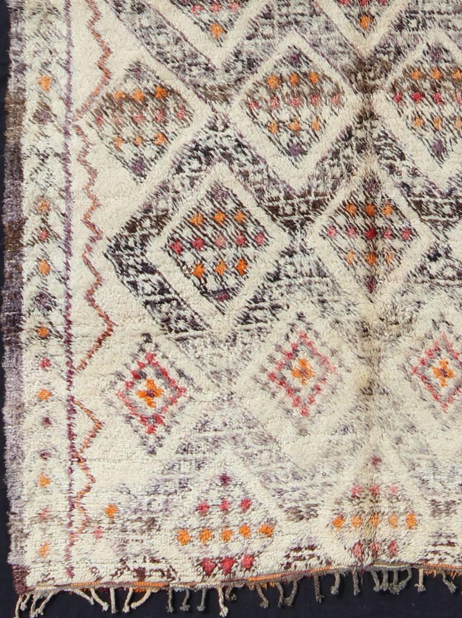 A gorgeously original vintage carpet from the eastern Middle Atlas mountains, this piece was woven in ivory/cream pure wool. It has delicate and complex tribal motifs embedded in an overall grid of hatched diamonds. Red and orange add depth to the