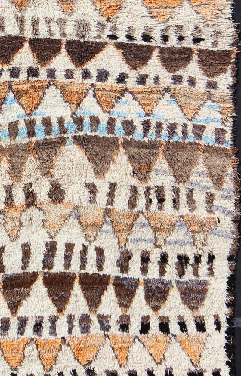 Measures: 6'7'' x 10'5''.
This piece is a large and unusual vintage Azilal rug from central Morocco, in the Atlas Mountains. The silky wool pile features natural cream and warm browns, along with muted orange motifs mixed with a row of sky blue. The
