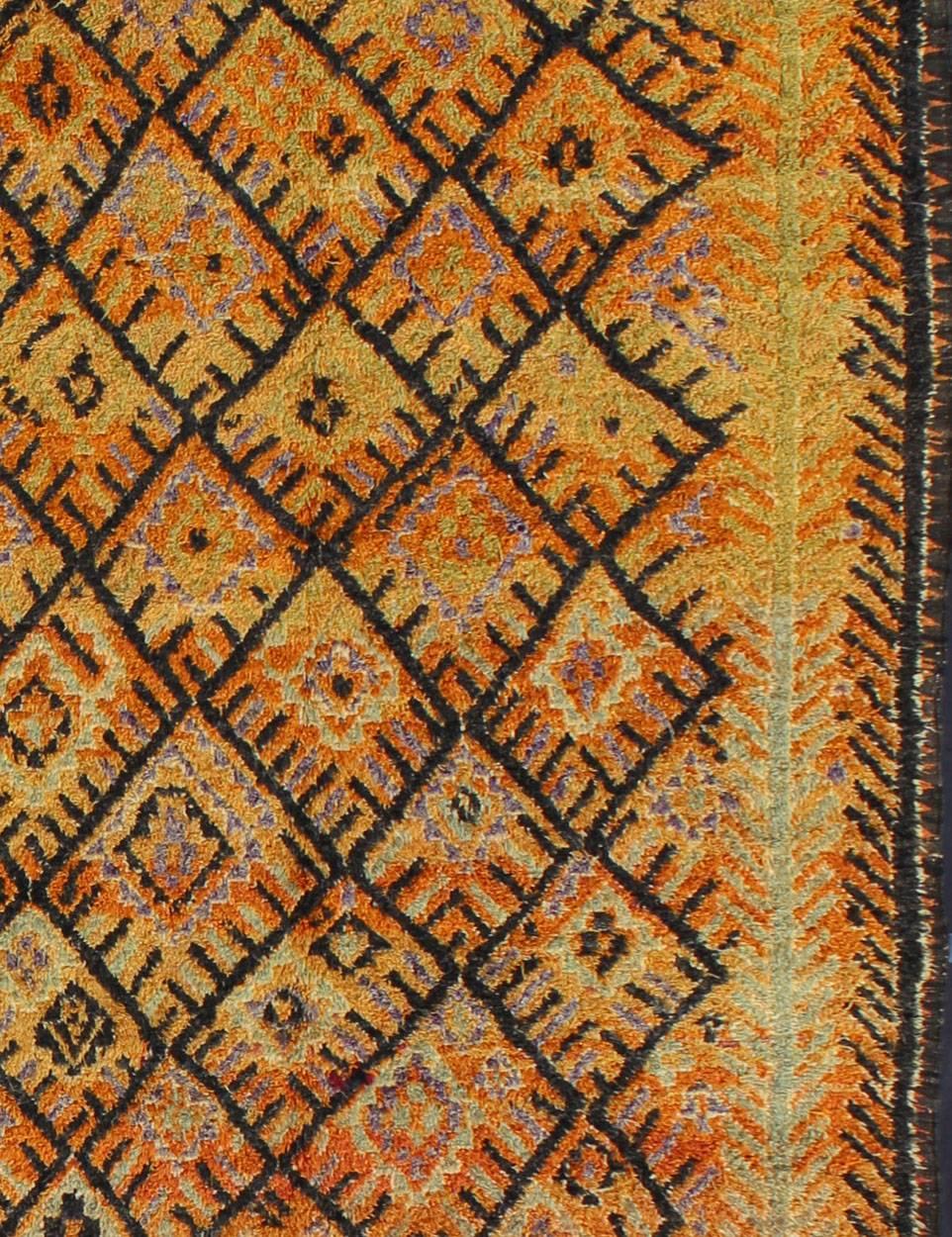 Measures: 6'6'' x 16'0''.
This vintage Moroccan rug was woven by the Moroccan Berber tribes of Talsint. A lovely gallery rug, it has a two long mint green vines that run on either side of the deep black diamond pattern. The rich orange alternates to