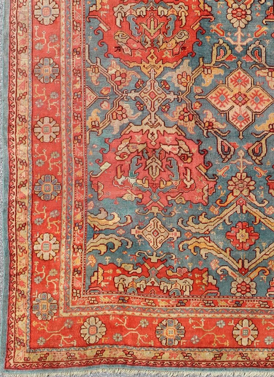 This wonderful Turkish Oushak rug is set on a teal-blue background. The eight over-sized medallions are opulent with two shades of coral and the same accent colors in the center field. The background features flower motifs with vine scrolls that