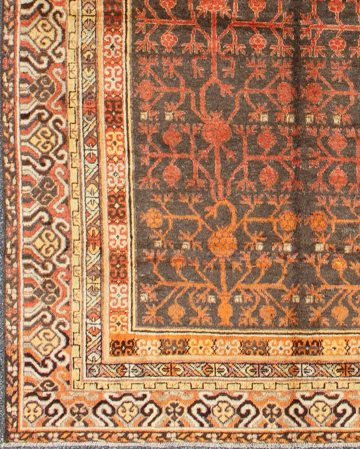 An antique, early 20th century, Central Asian Khotan rug with traditional all-over pomegranate pattern on a charcoal field surrounded by multiple complementary floral borders of gold and orange. 
Measures: 5'7 x 8'11.