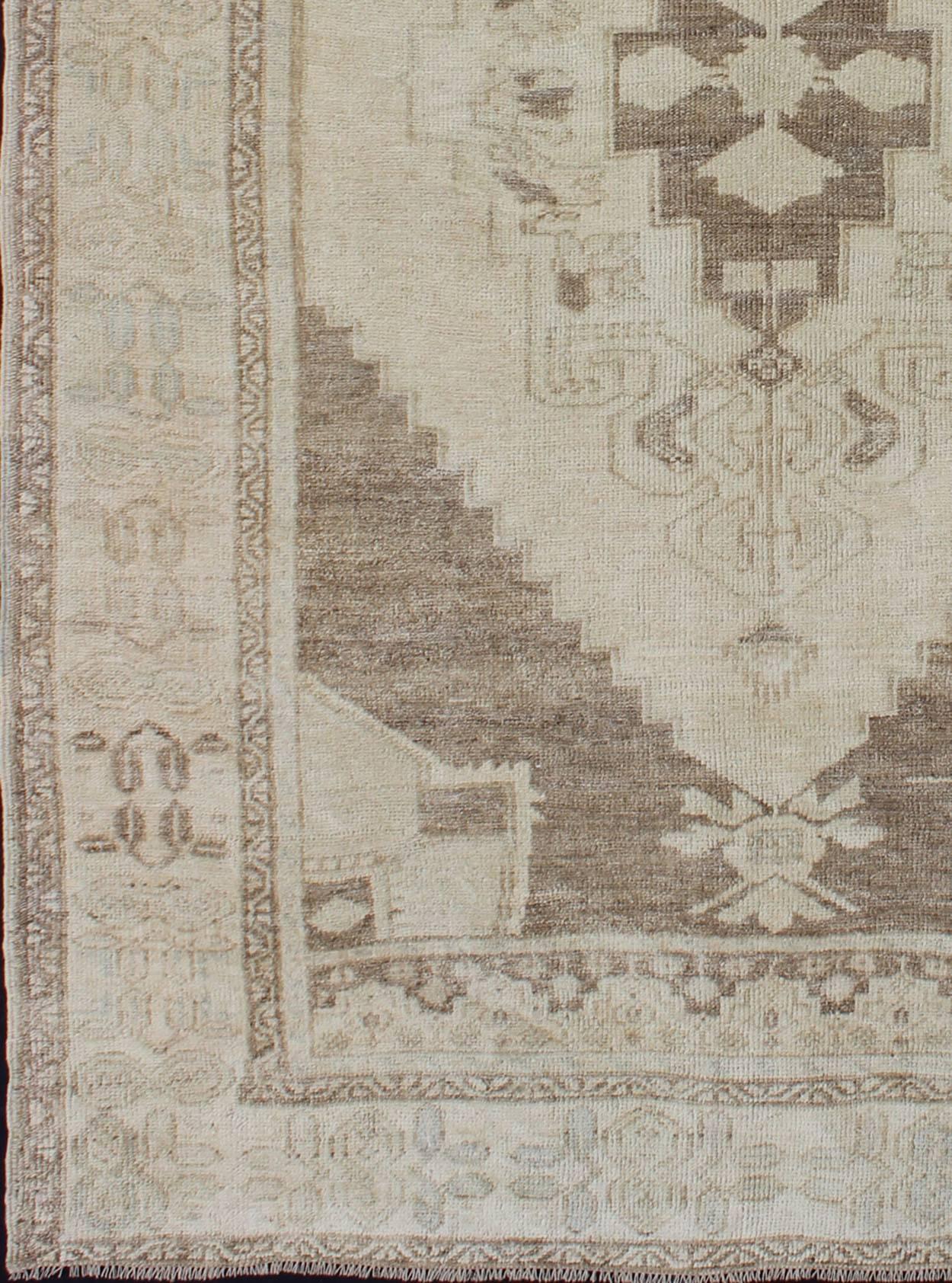 This vintage Oushak beautifully illustrates the impressive craftsmanship and design of Turkish weavers. The large medallion flows through the center field of taupe, light blue and green hues. Linear branches on either side of the medallion extend