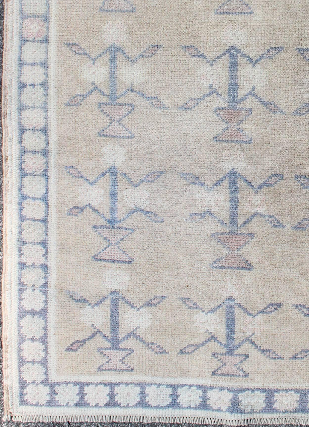 This Tulu carpet features several blue tribal motifs laid across a sand-colored field and enclosed within a blue border of alternating botanical motifs. Accent colors include ivory, taupe, and cream. Tulus are woven in the Konya area with a very