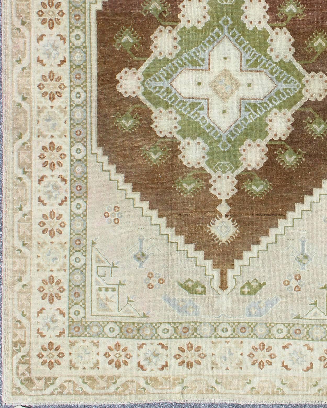This Oushak rug features a unique blend of colors and an intricately beautiful design. The multi-layered diamond medallions are complemented by a symmetrical set of floral motifs. The various shades of ivory, taupe and cream blend beautifully with