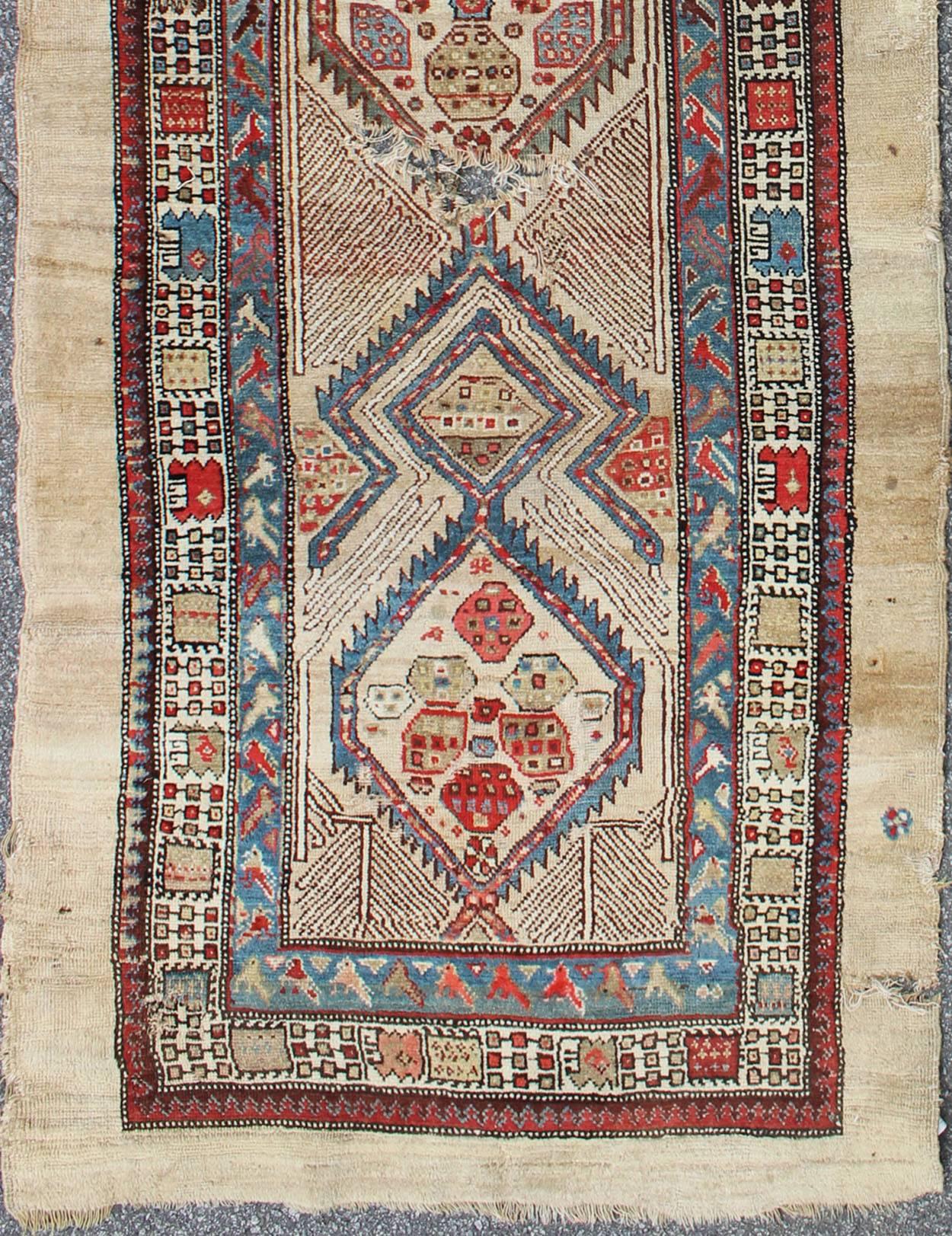 This beautiful antique Serab, antique mid-19th century Persian Serab, runner rests on a camel background, which surrounds the three medallions of alternating ivory, red, and blue colors. The main border is composed of ivory with a repeating