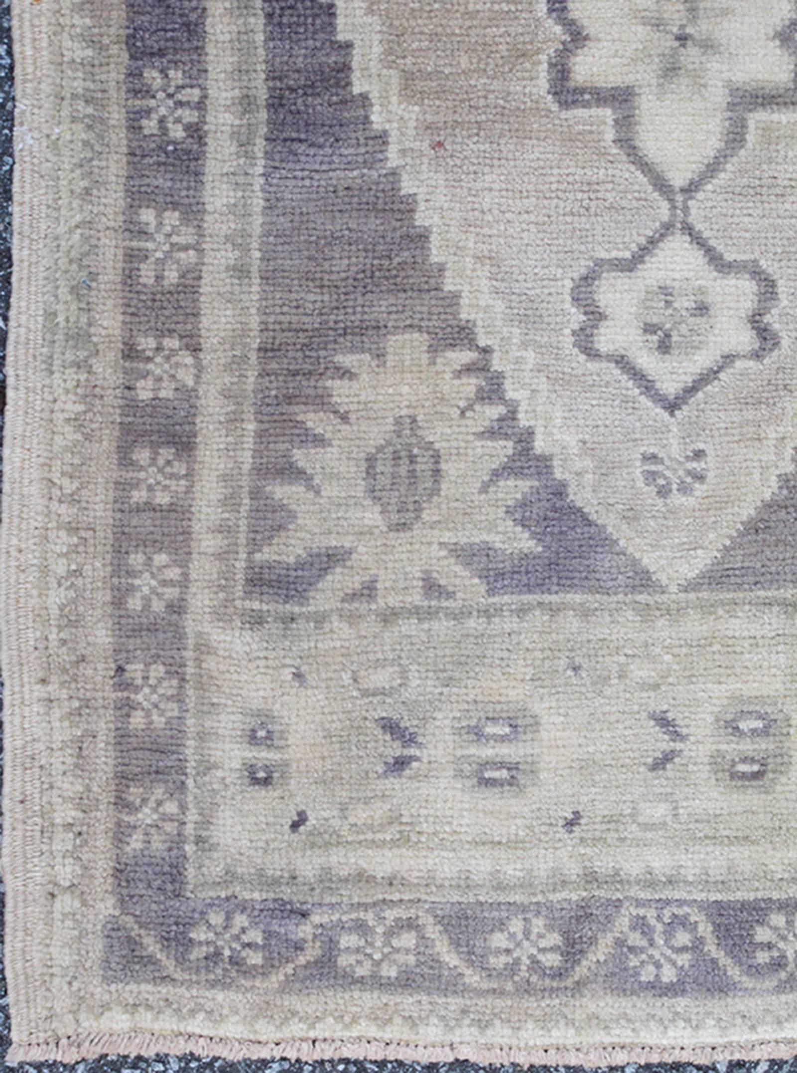 This Turkish Oushak carpet features a central medallion design, as well as patterns of smaller geometric shapes and botanical elements. The rug's qualities are enhanced by its particularly soft and lustrous wool. Colors include dark gray/purple,