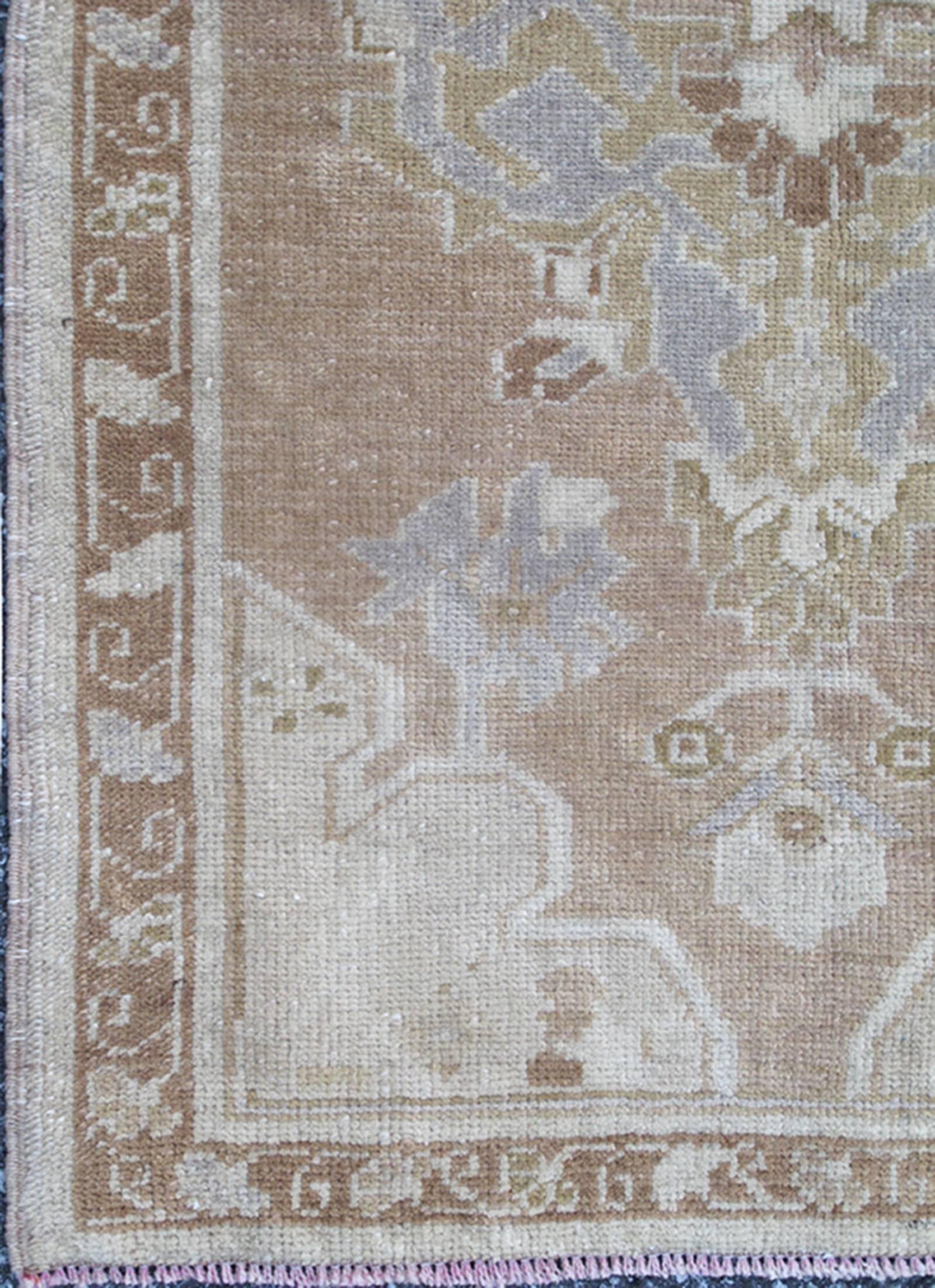 This Turkish Oushak carpet features a central medallion design, as well as patterns of smaller geometric shapes and botanical elements. The rug's qualities are enhanced by its particularly soft and lustrous wool. Colors include medium and light