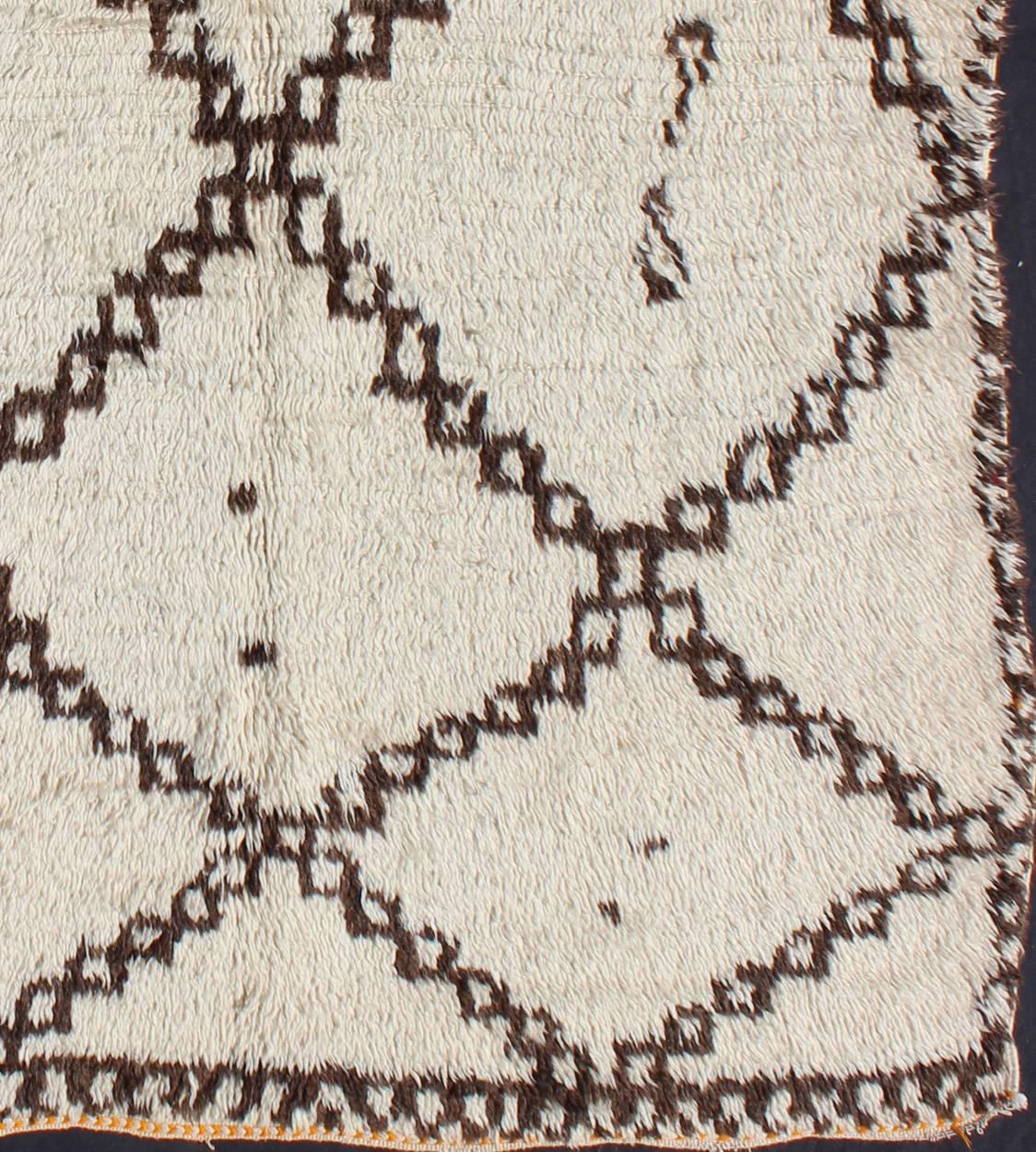 Measures: 4'10'' x 7'0''.
This graphic handwoven, tribal Beni Ourain rug features an all-over design of large, interconnected diamond shapes, some of which host tribal figures in their centers. The white/ivory is soft, pure wool while the design is