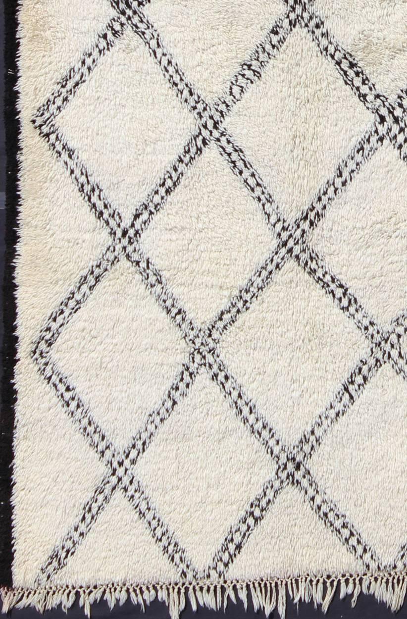 Measures: 6'6'' x 11'0''.
This graphic handwoven, tribal Beni Ourain rug features an all-over design of large, interconnected diamond shapes; three of which stand out in the center due to their smaller shape. The white/ivory is soft, pure wool while