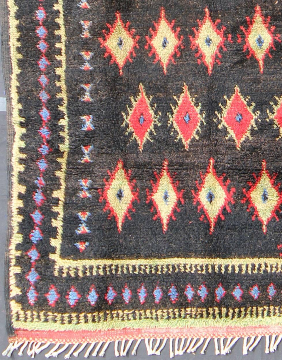 Measures: 4'9'' x 9'10''.
Featuring a central charcoal field full of red and yellow diamond-shaped motifs, this unique Moroccan rug displays a harmonious and rich color palette of charcoal, red, cream, yellow and blue. Its border is composed of