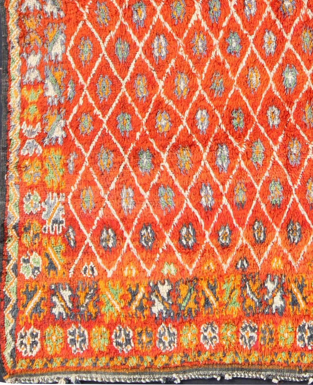 Measures: 6'9'' x 9'0''.
This Moroccan rug has an all-over diamond geometric pattern with ivory outlines, set on a field shaded with orange and red. The border features various sub-geometric motifs. Colors include ivory, charcoal, orange, red, gray