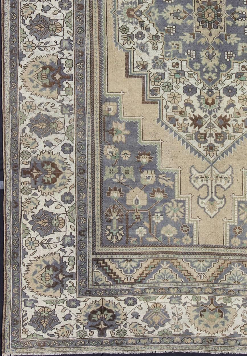 Measures: 8'0'' x 12'8''.
This antique Turkish Oushak carpet (circa mid-20th century) features a central medallion design, as well as patterns of smaller floral elements in the four cornices and in the borders. The rug's qualities are enhanced by