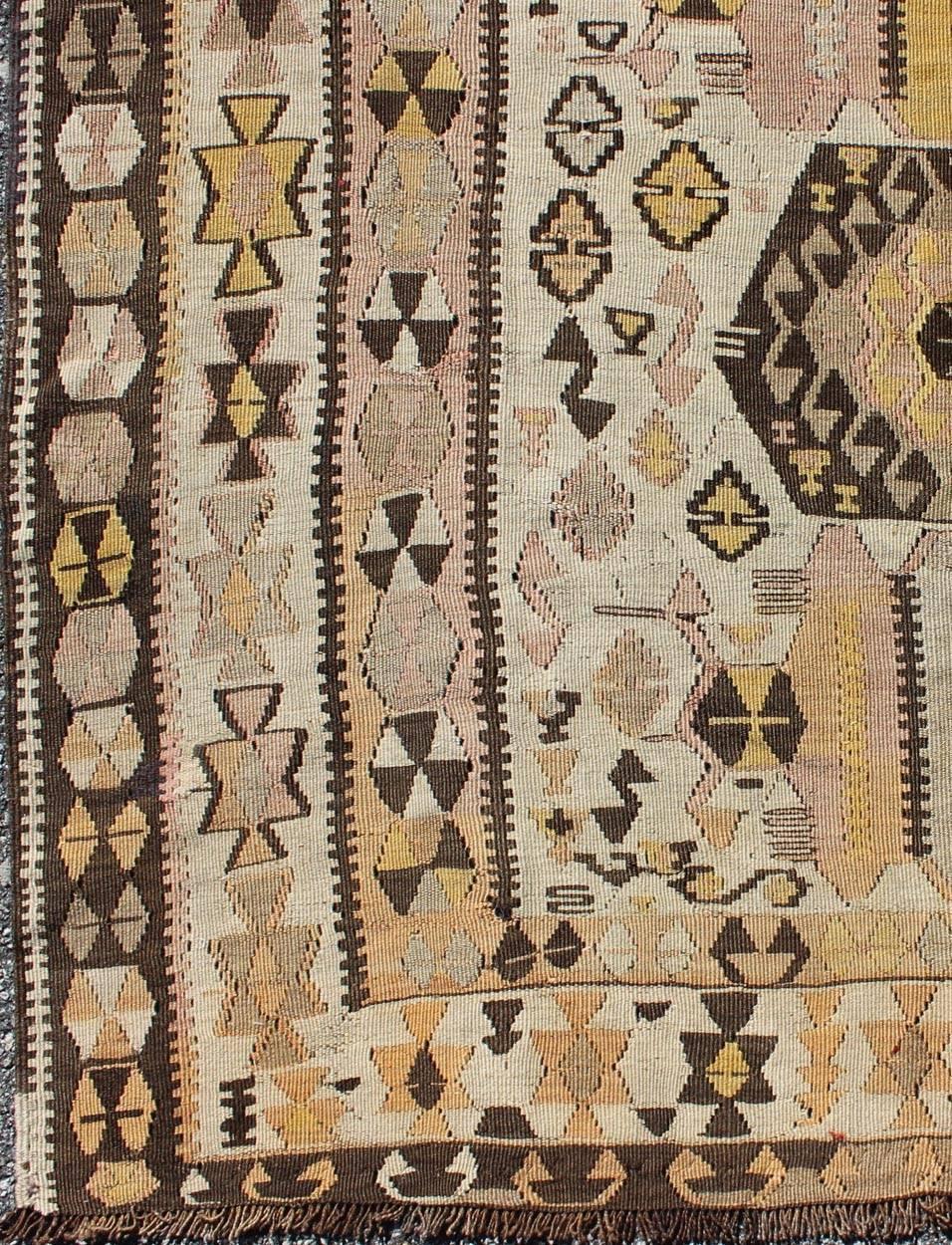 Ce tapis Kilim turc vintage (vers le milieu du 20e siècle) présente un mélange unique de couleurs et un beau design complexe. Les médaillons centraux consistent en une ligne verticale de tribus, entourée de figures complémentaires dans le champ et