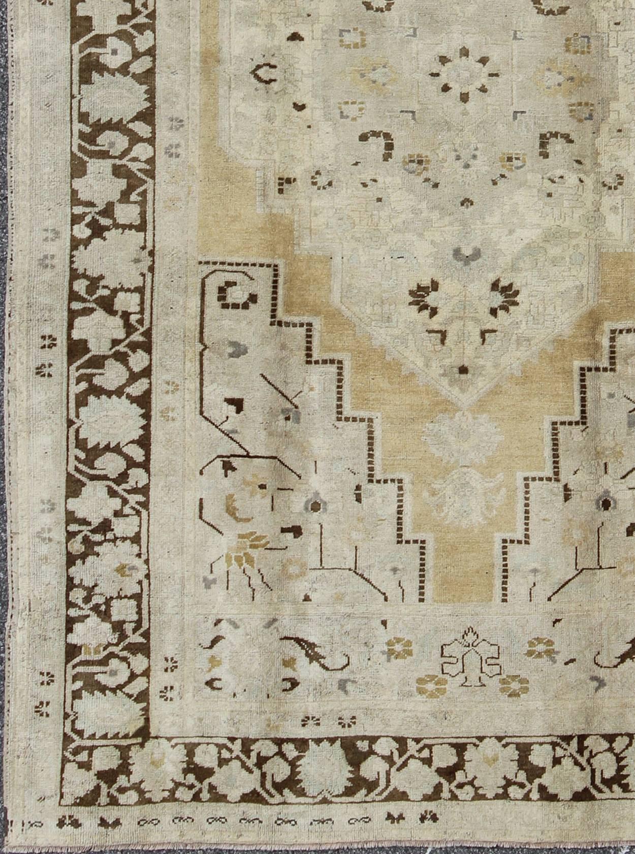 Turkish Oushak Rug in Pale Yellow, Taupe and Brown Border.
This softly muted Oushak carpet rests beautifully upon a field of elegant golden taupe. A large medallion takes center stage and is well balanced by four prominent organic corner motifs
