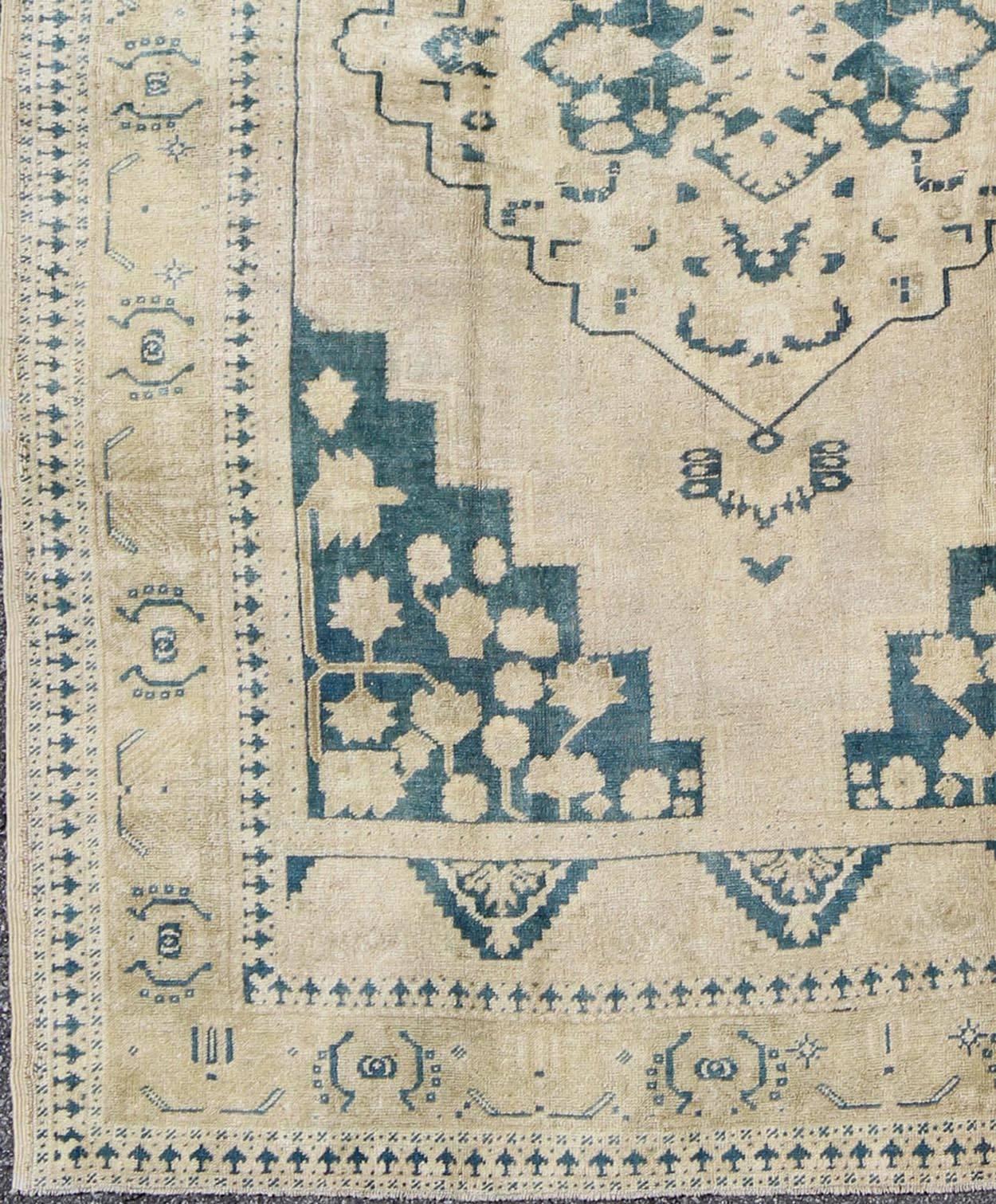 This geometric Turkish Oushak carpet rests beautifully upon an ivory background with a cream border. A blue outlined medallion takes center stage and is well balanced by four organic corner motifs composed of the same blue and neutral colors.