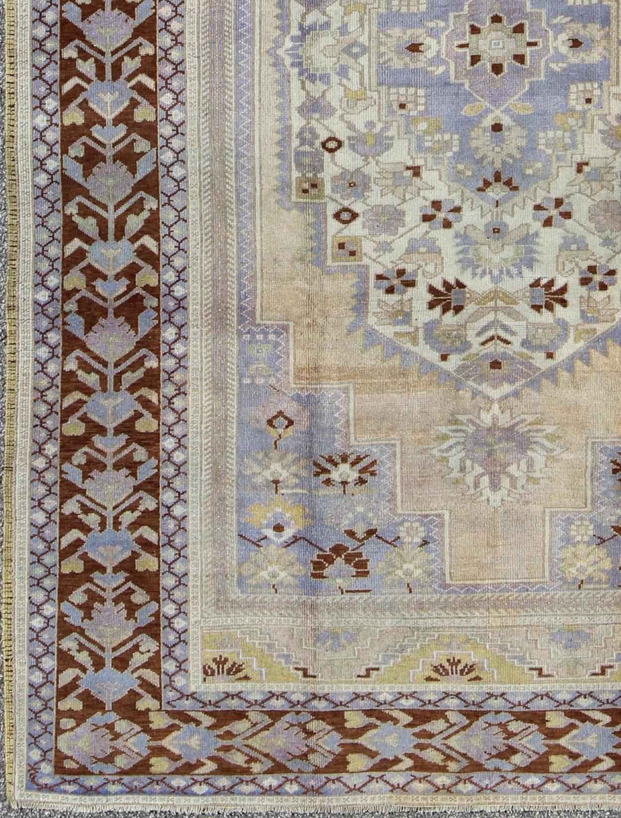 Vintage Turkish Oushak Rug in Brown, Light Purple, Blue, Camel and Wheat Colors.
This unique vintage Turkish Oushak rug shows a charming combination of warm and cool colors. Set on a brown border with a pop of the same brown throughout, this unique