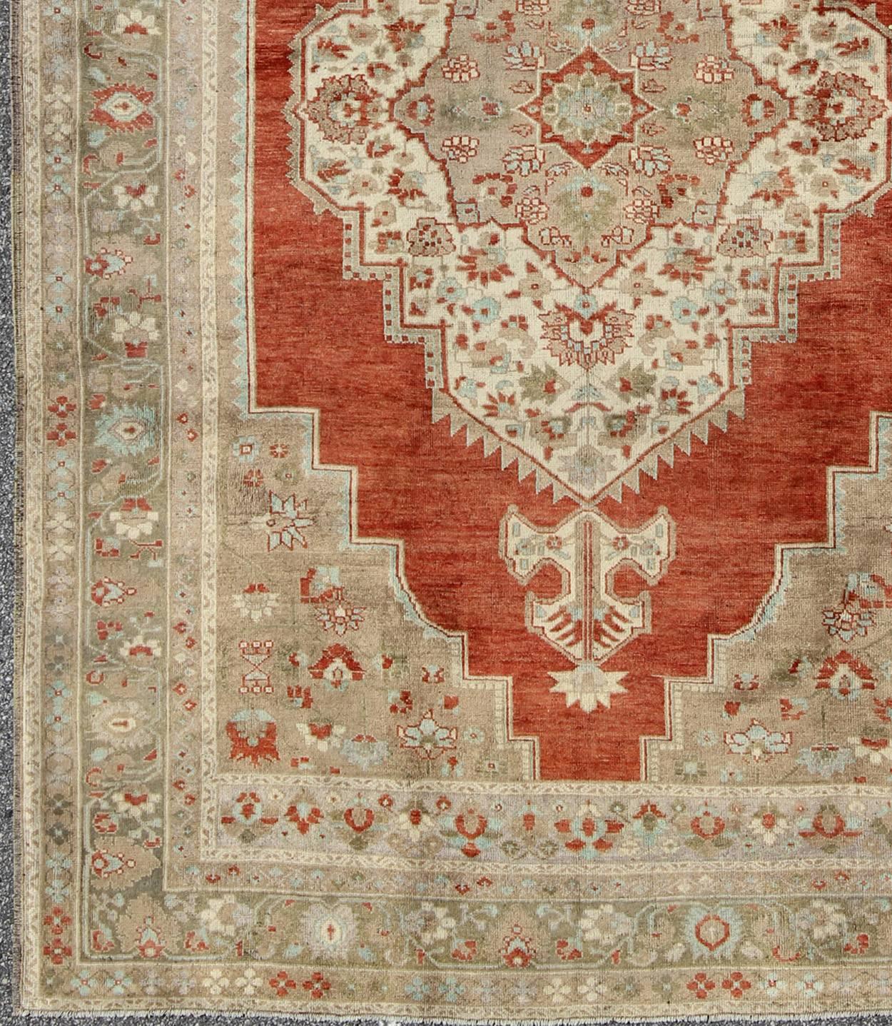 This beautiful classic vintage Oushak has a large medallion in rust/orange red complemented by light green border and warm taupe and cream colors. The medallion is enclosed by a complementary bored, making this rug quite well suited for traditional,