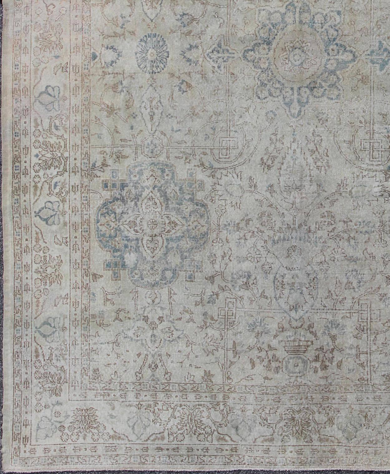 This beautiful Oushak carpet showcases the skillful workmanship of Turkish weavers. Set on an all-over ivory background, this piece consists of sublimely delicate patterns of palmettes and arabesque tendrils in soft tones of blue, camel and wheat,