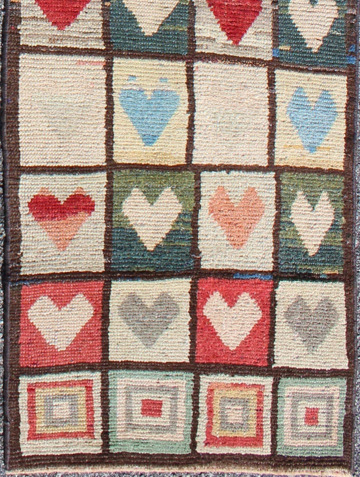 This arty Tulu boasts a unique heart-shaped pattern. The various tones of light blue, red, gray, pink, forest green, and cream blend superbly to emphasize the exceptional color scheme. The chocolate border transitions to a lighter brown tone along