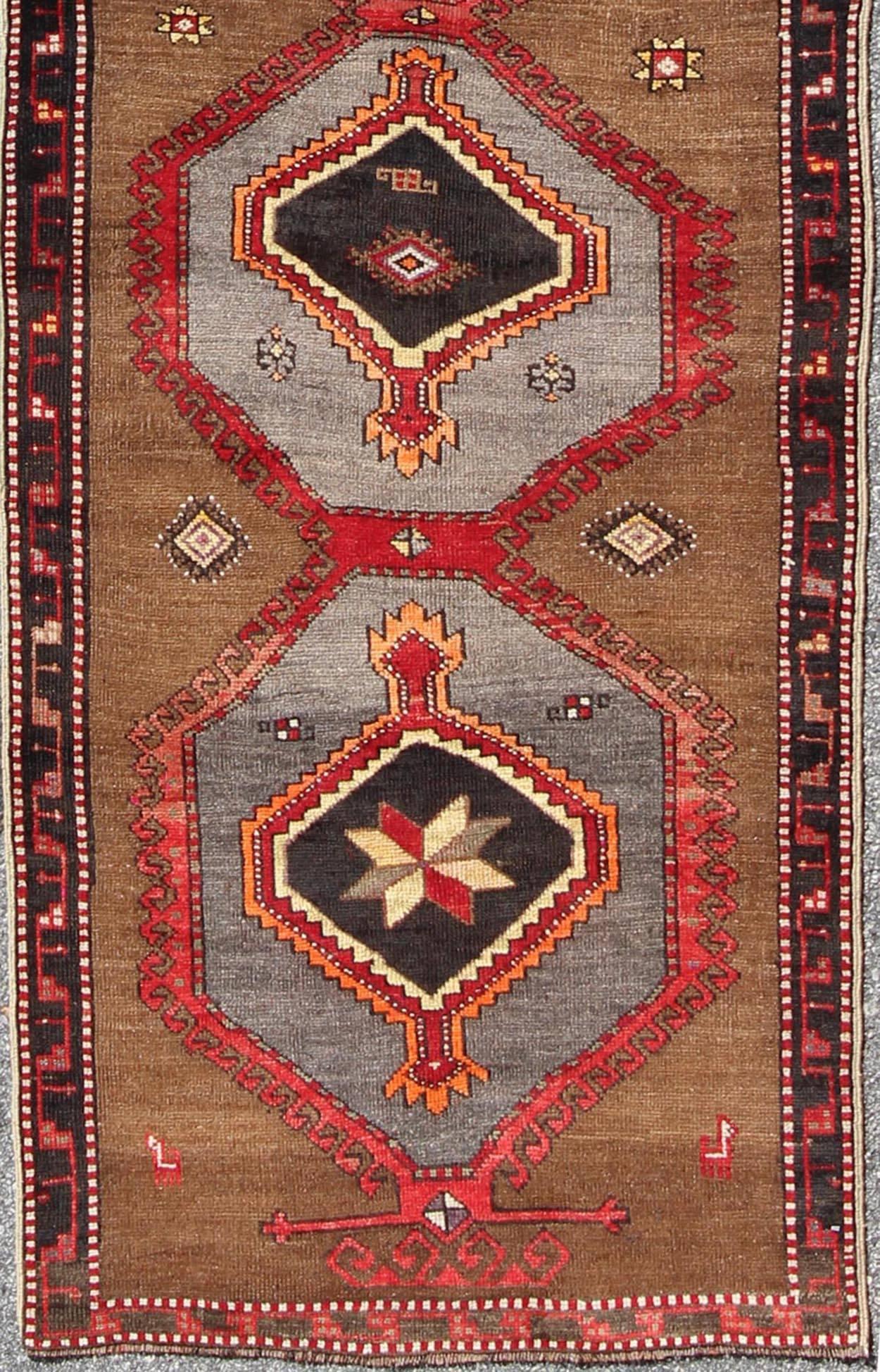This Turkish runner boasts five geometric medallions along with a unique color scheme. The light and dark shades of brown in the background surround the multi-diamond shaped geometric medallions. The multi-color medallions contrast beautifully with