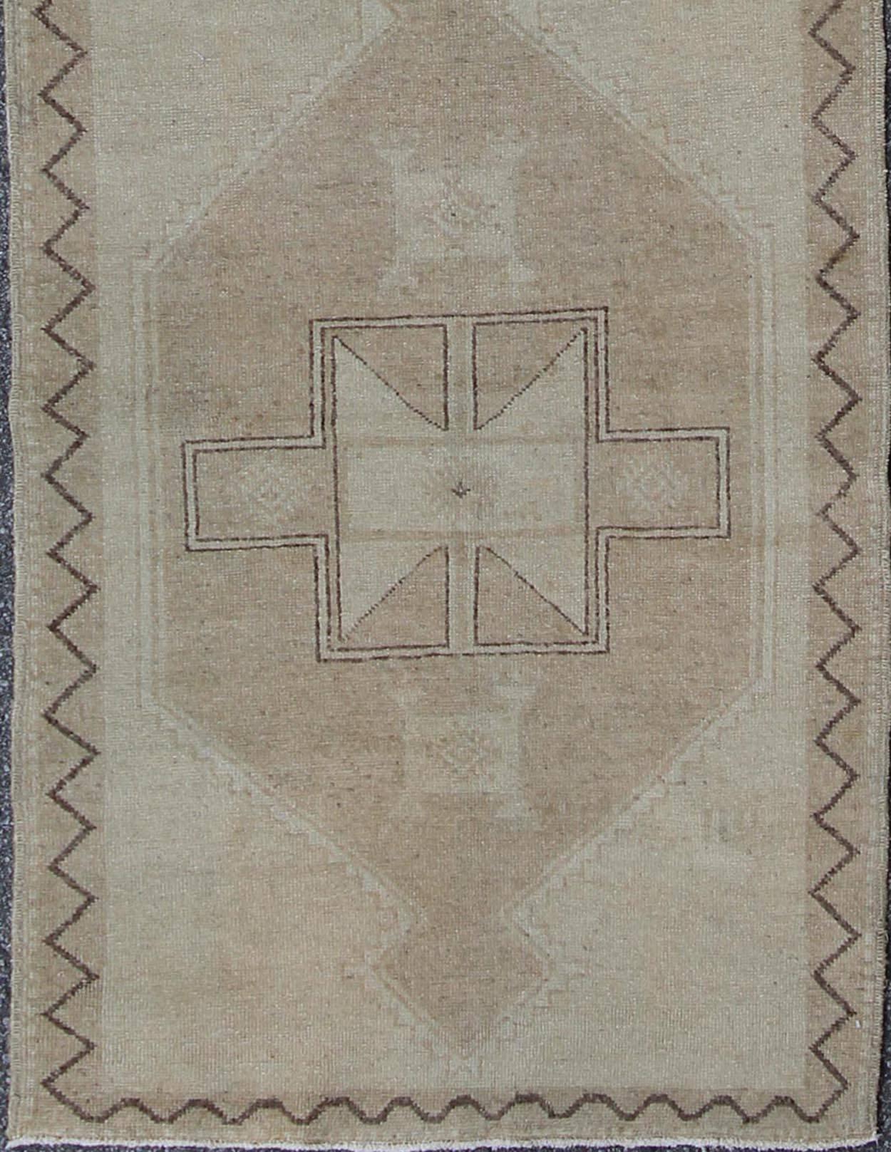 This Oushak runner presents three unique medallions laid out across a solid beige field. Each medallion contains a variation of taupe, beige, tan, cream, and brown, which blend together to accentuate its delicate geometrical design. A slightly
